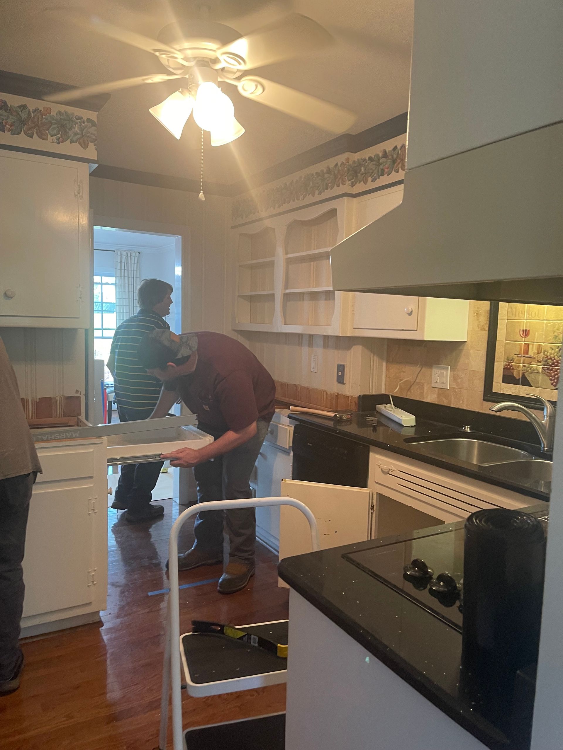 Two people working in a bright kitchen, one bending over a cart near the sink
