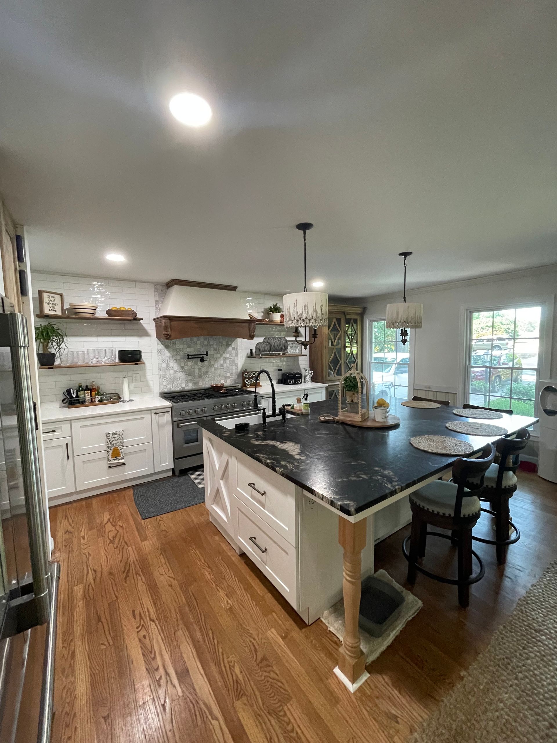 Bright kitchen with black island, white cabinets, wood floors, and a dining table by a window.