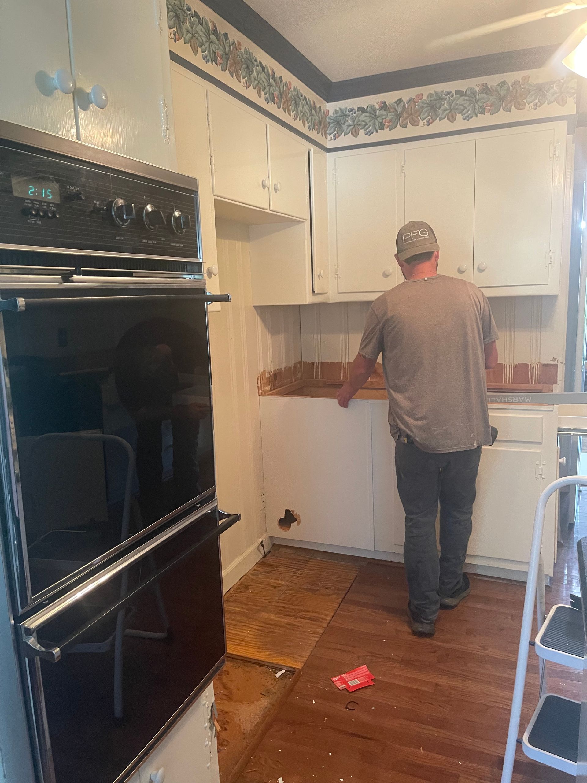 Person standing in a small kitchen, facing cabinets and countertop near a black oven.