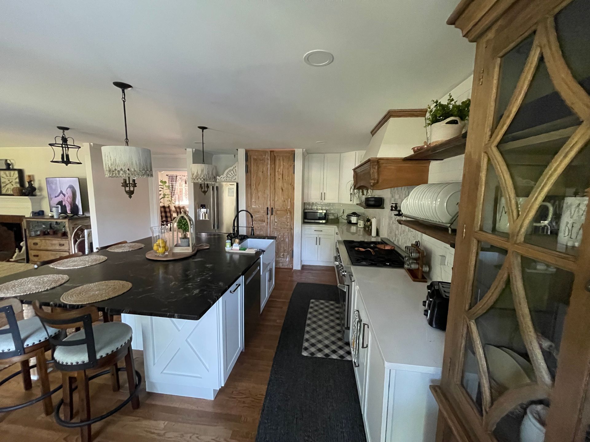 Bright kitchen with black island, white cabinets, wood floors, and a decorative glass cabinet.