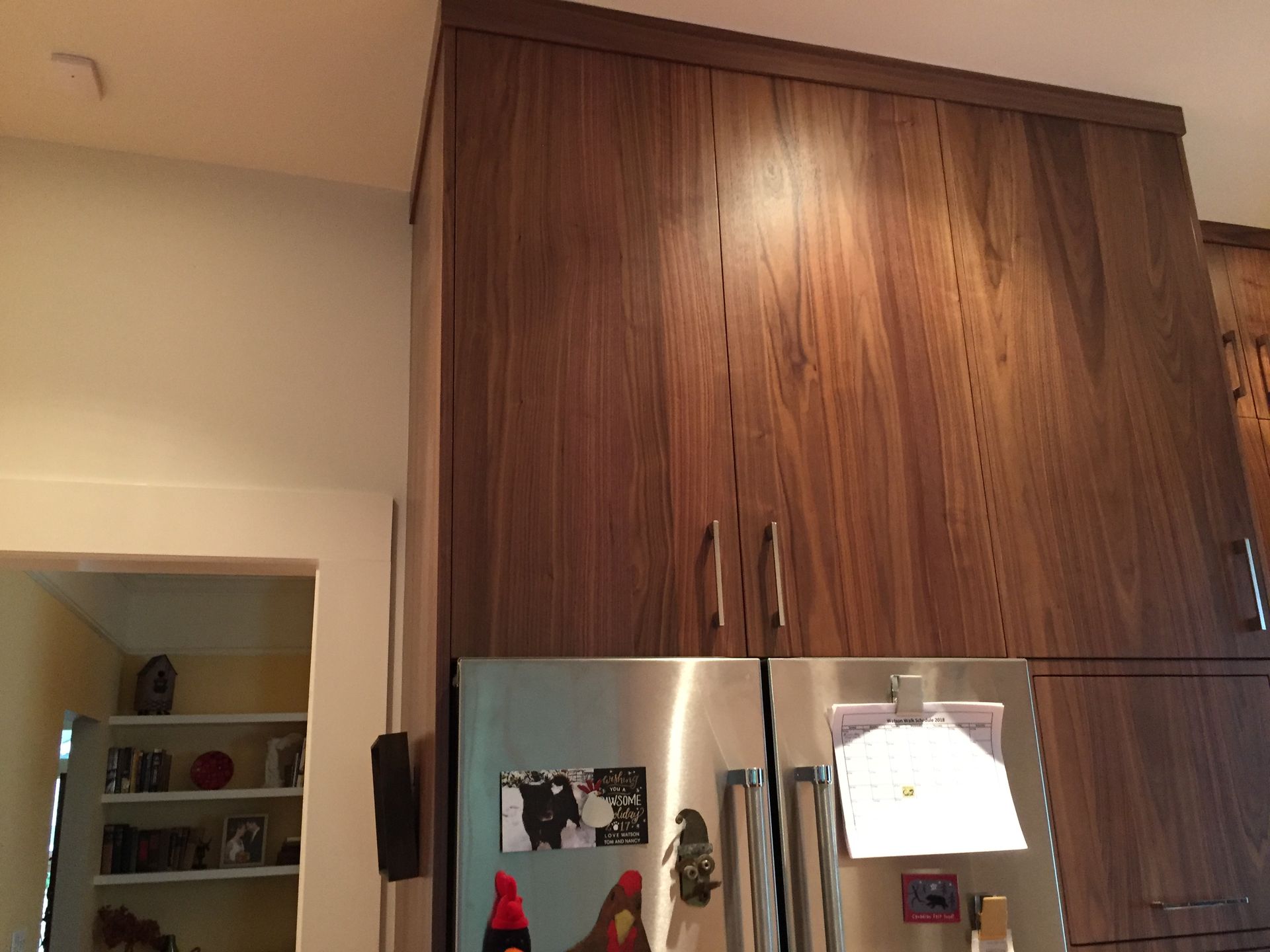 Kitchen with tall dark wood cabinets above a stainless steel refrigerator and a doorway to the left