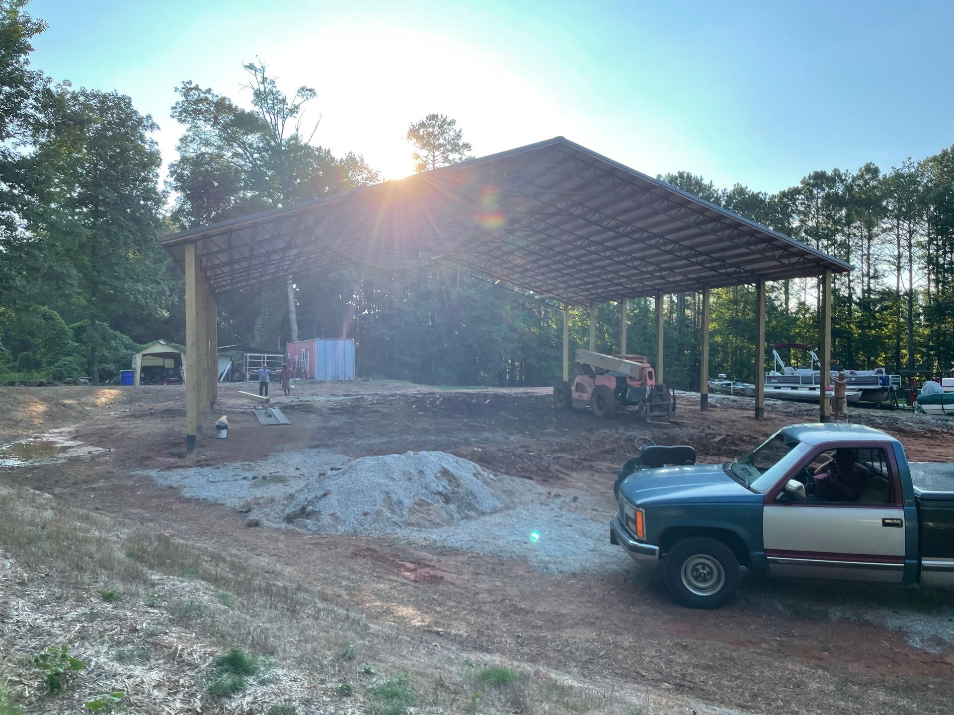 Blue pickup truck beside a large open-sided pavilion under construction at sunset