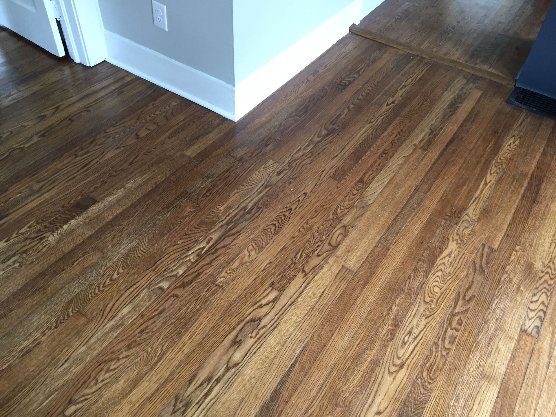 Empty room corner with brown wood flooring and white walls, lit by daylight.
