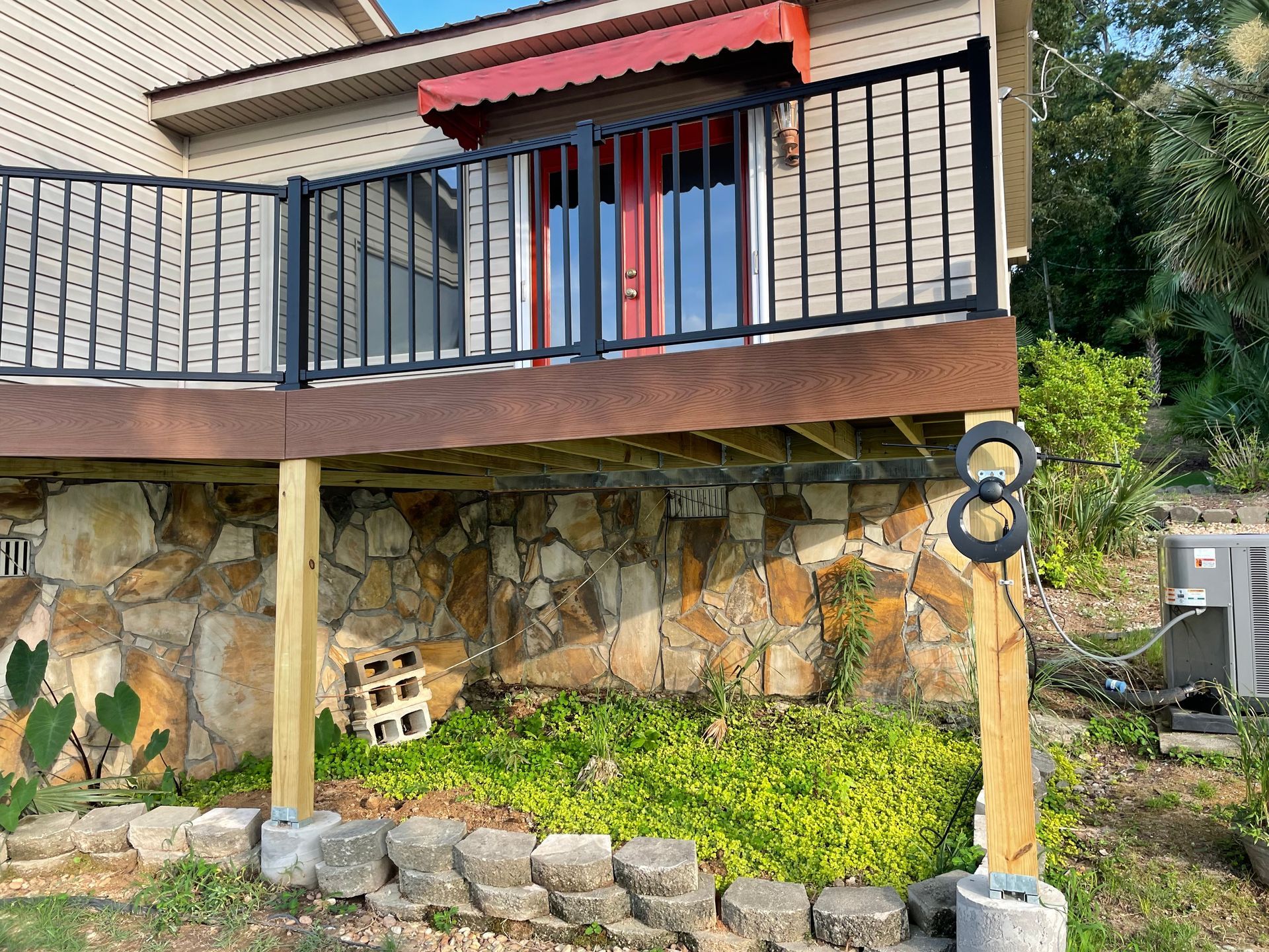 House exterior with stone foundation, black balcony railing, red awning, and a landscaped front garden