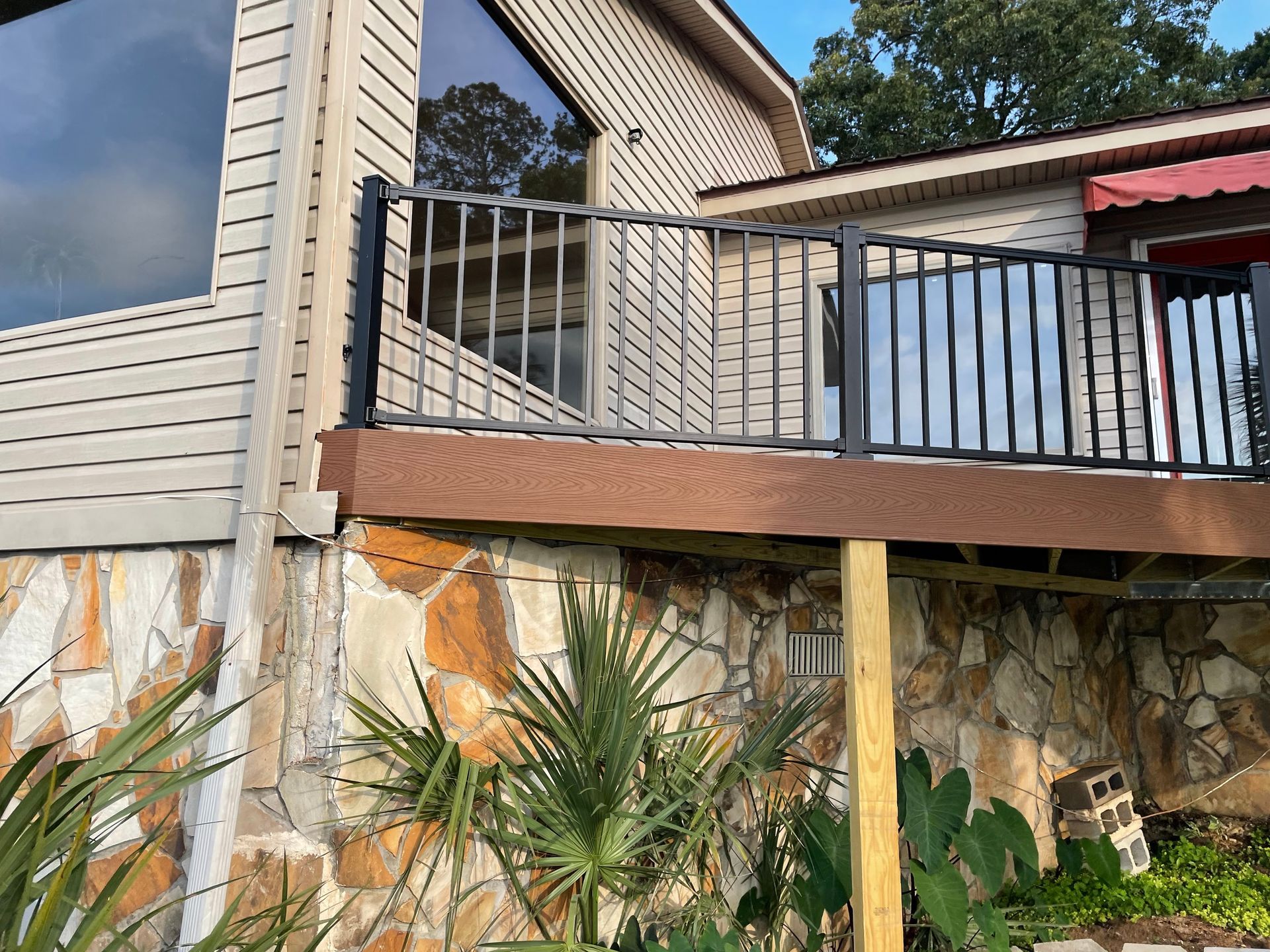 House deck with black railing over a stone retaining wall and palm plants below