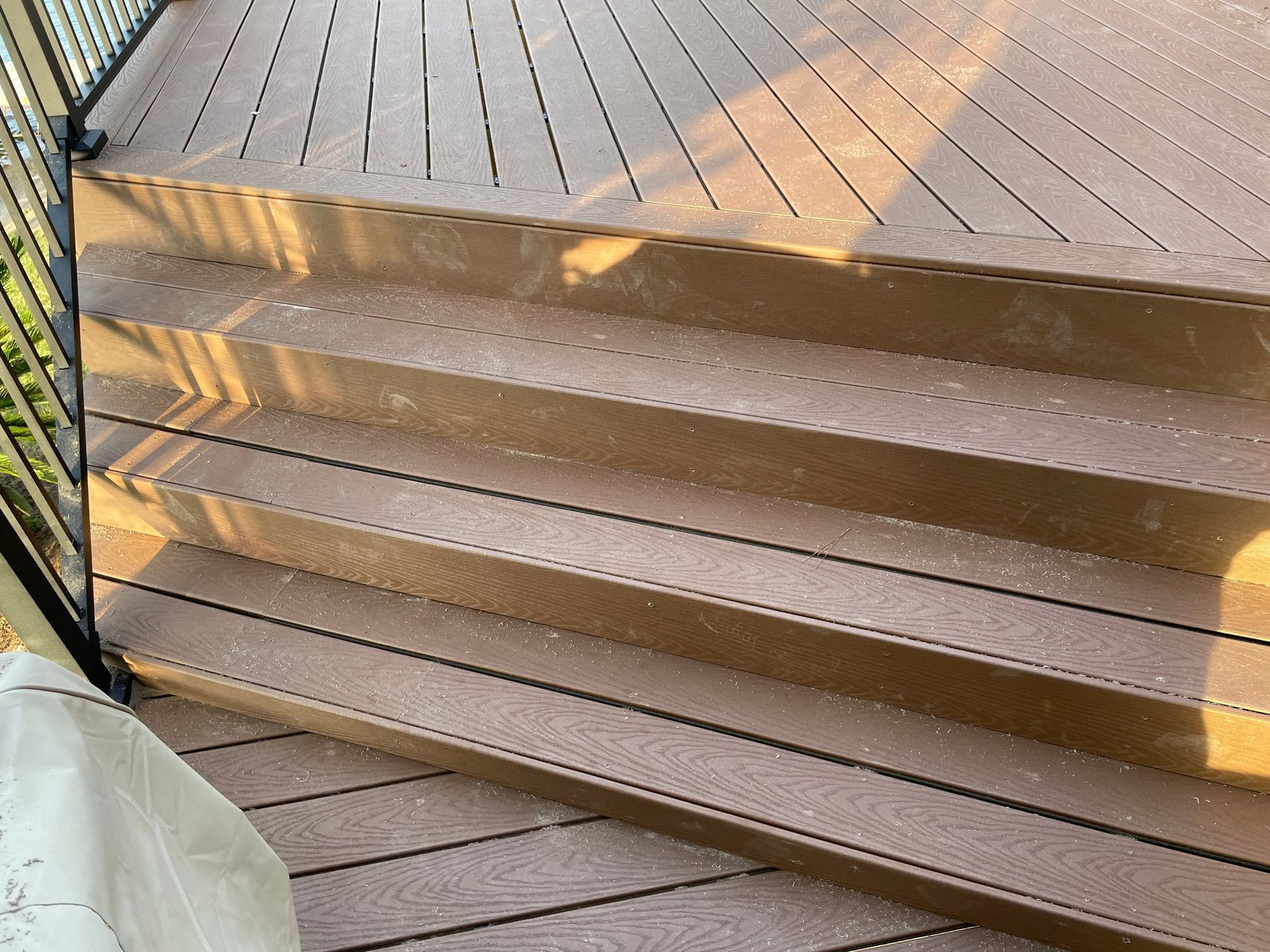 Brown wooden steps leading to a sunlit deck, with a white cushion at the lower left.