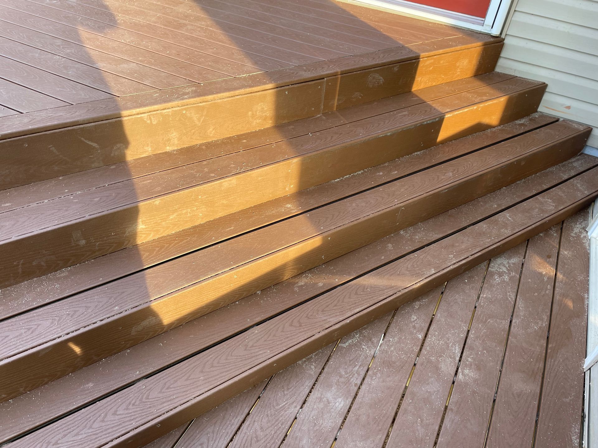 Brown wooden deck steps leading to a doorway, with a sunlit yellow stripe across the stairs.