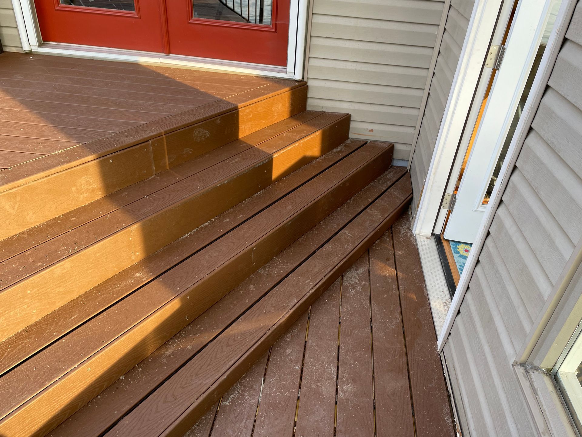 Brown wooden steps and porch beside a white-sided house with red doors and a small ramp