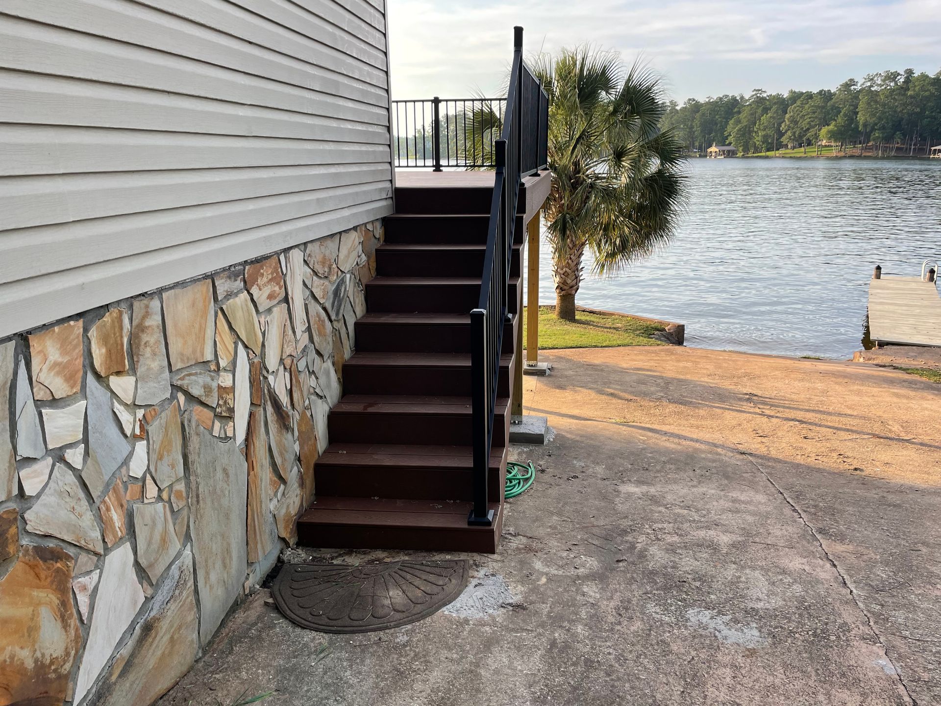 Outdoor stairs beside a house leading down to a lakeside concrete patio and dock area
