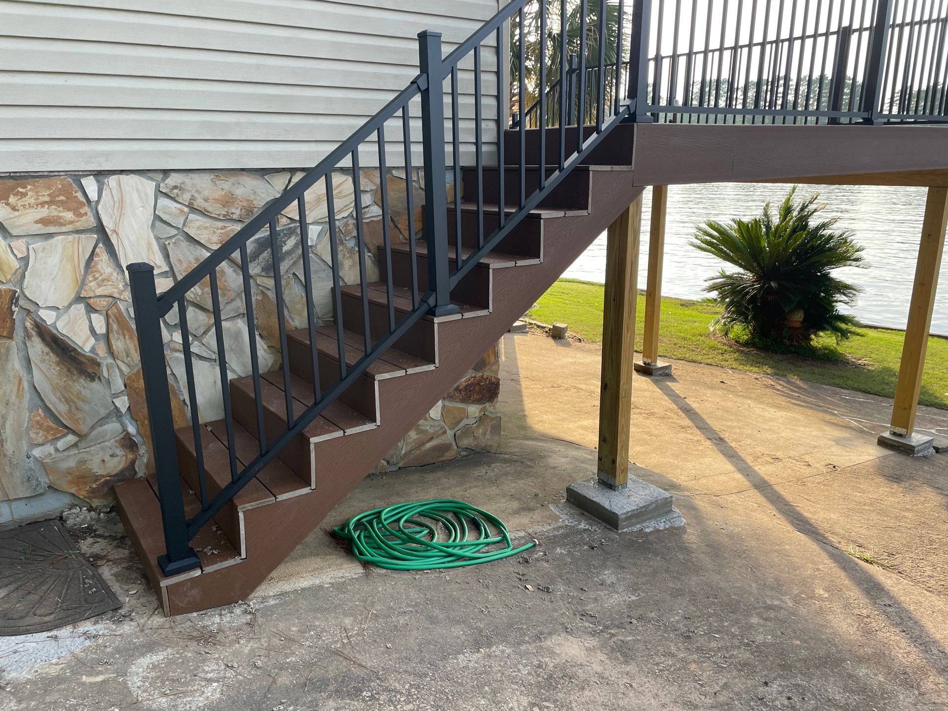 Exterior metal staircase beside a house, with a coiled green hose on the gravel below.