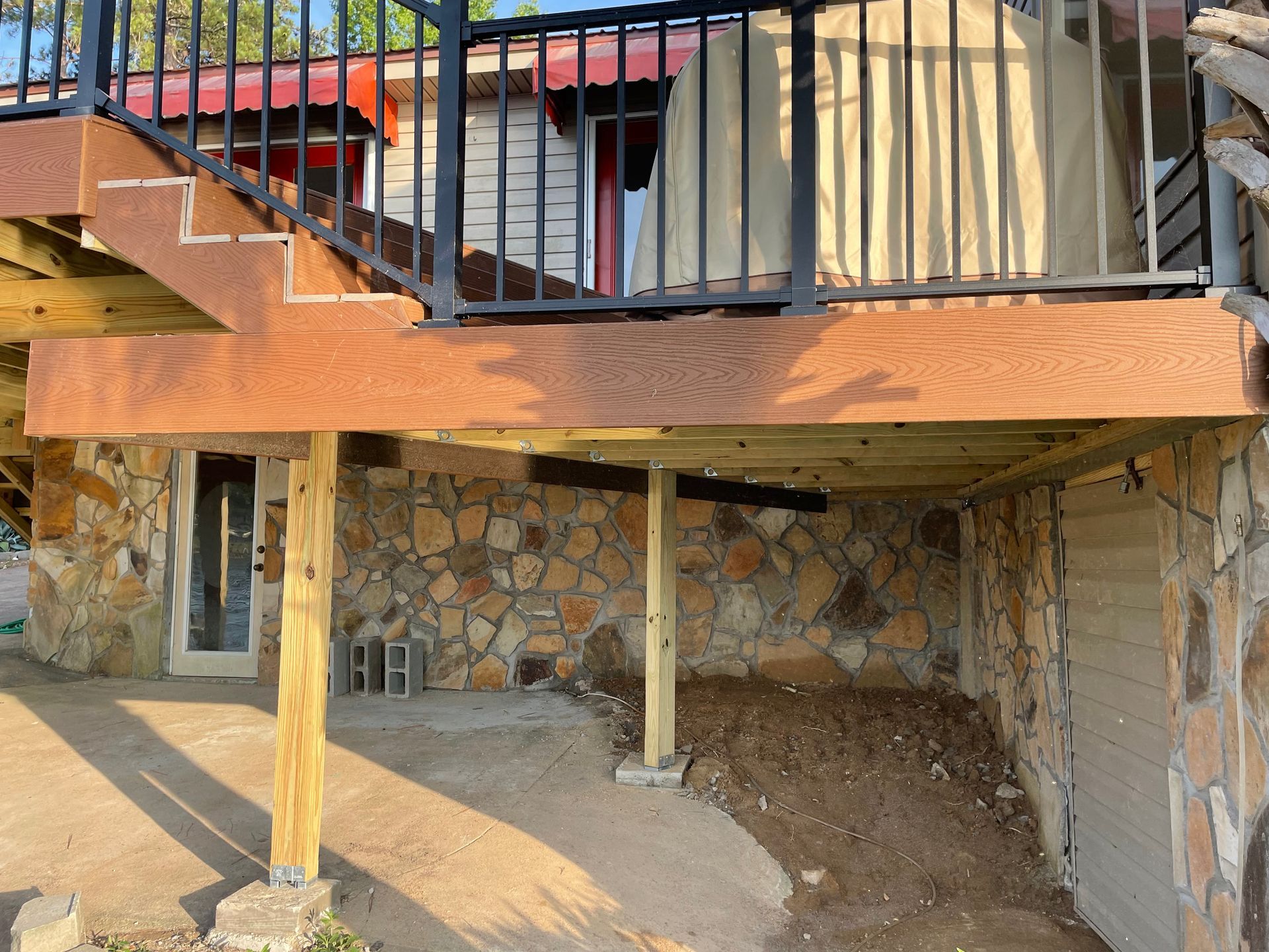 Staircase and deck with black railings above a stone wall, over a dirt undercroft area