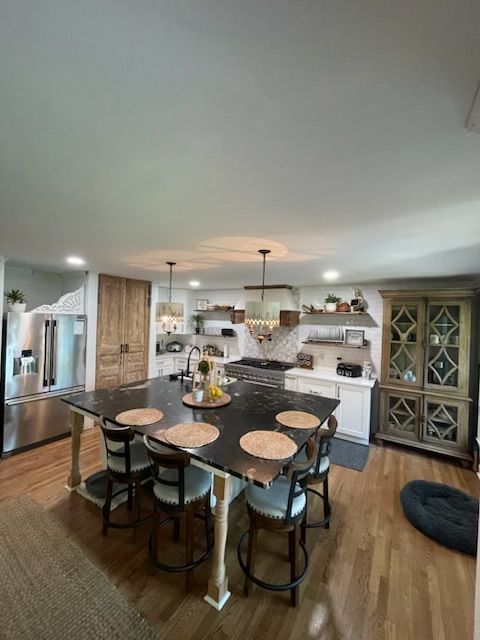 Open kitchen and dining area with dark table, wood floors, white cabinets, and glass display cabinet