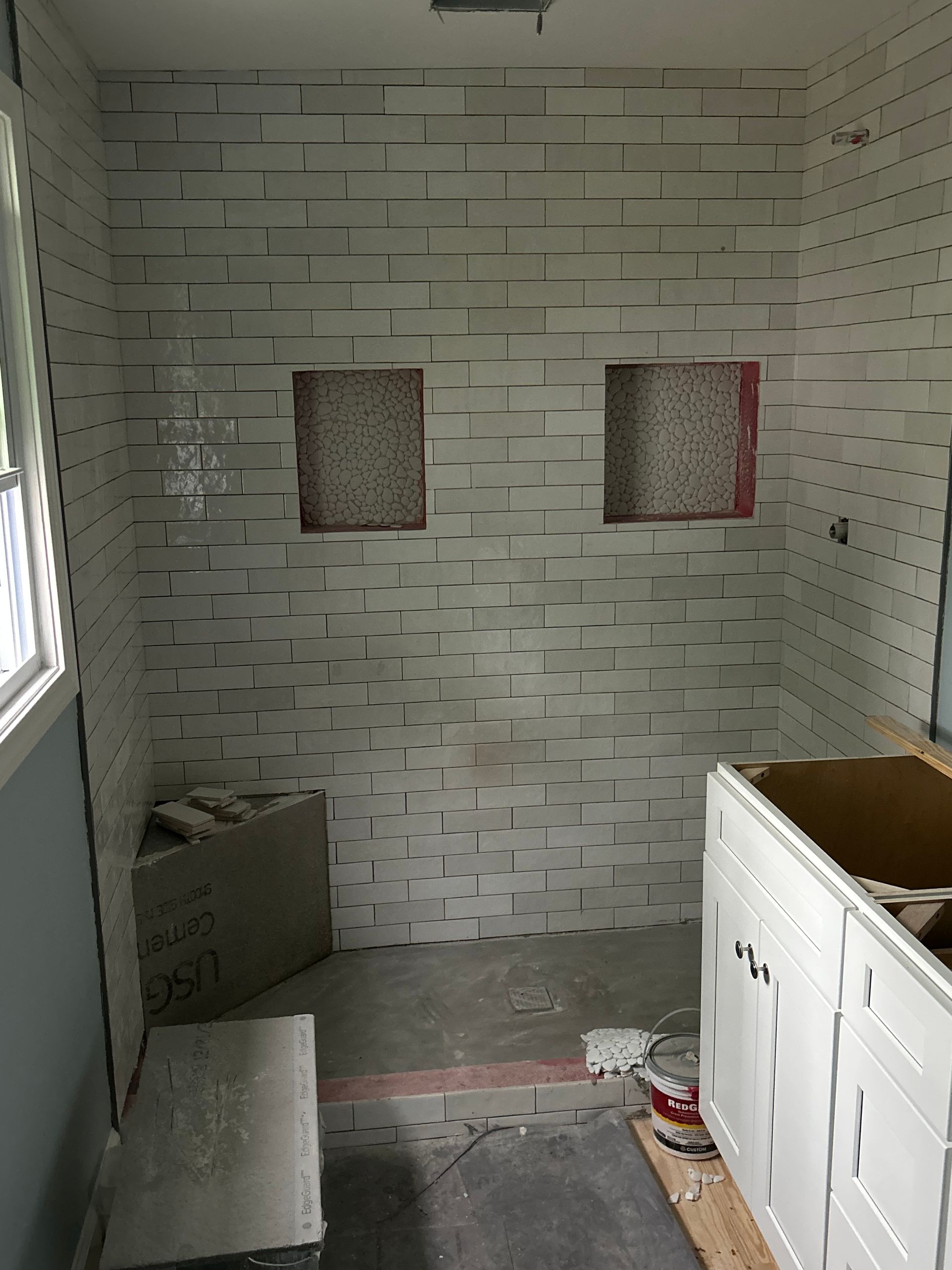 Small bathroom under renovation with tiled walls, two recessed niches, and a vanity cabinet.