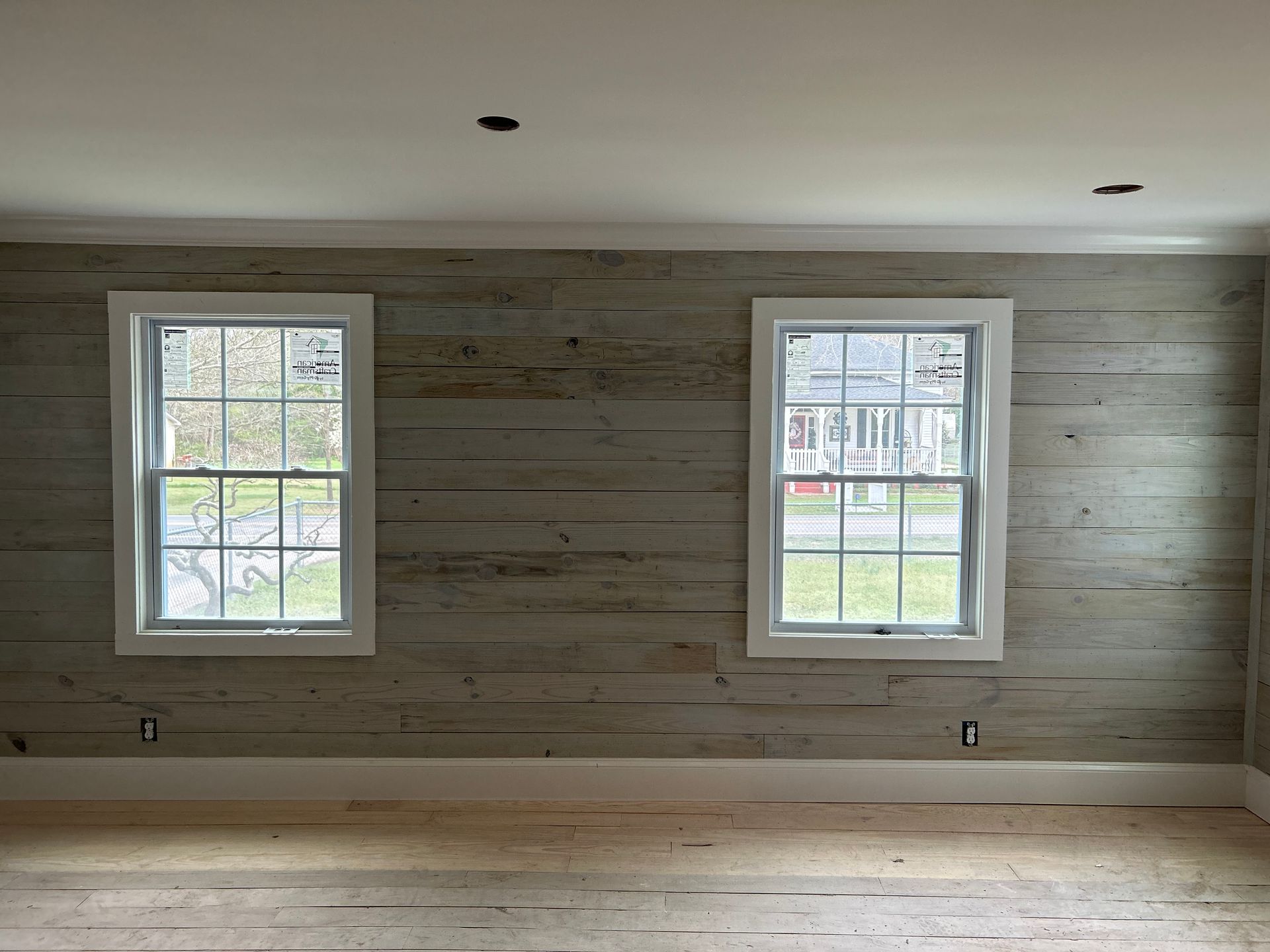 Empty room with white shiplap walls, two windows, and light wood floors