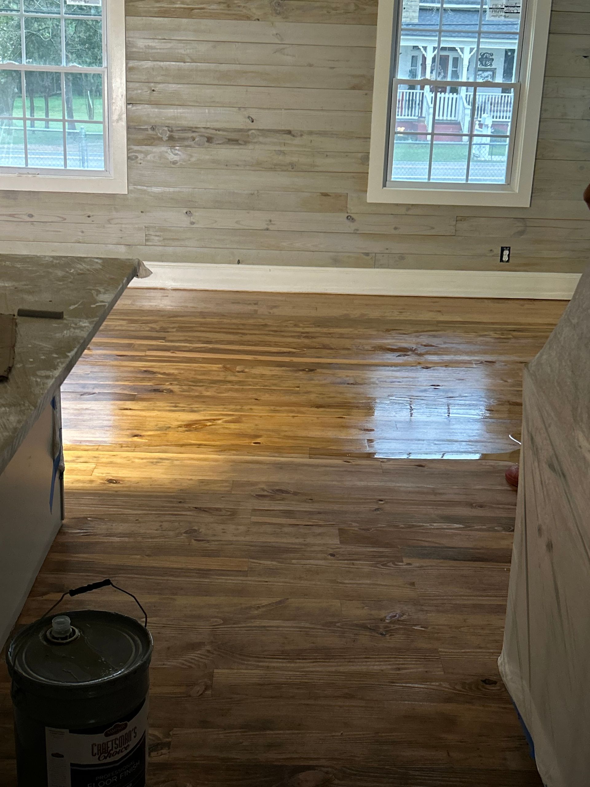 Freshly finished hardwood floor in a room with wood-paneled walls and two windows