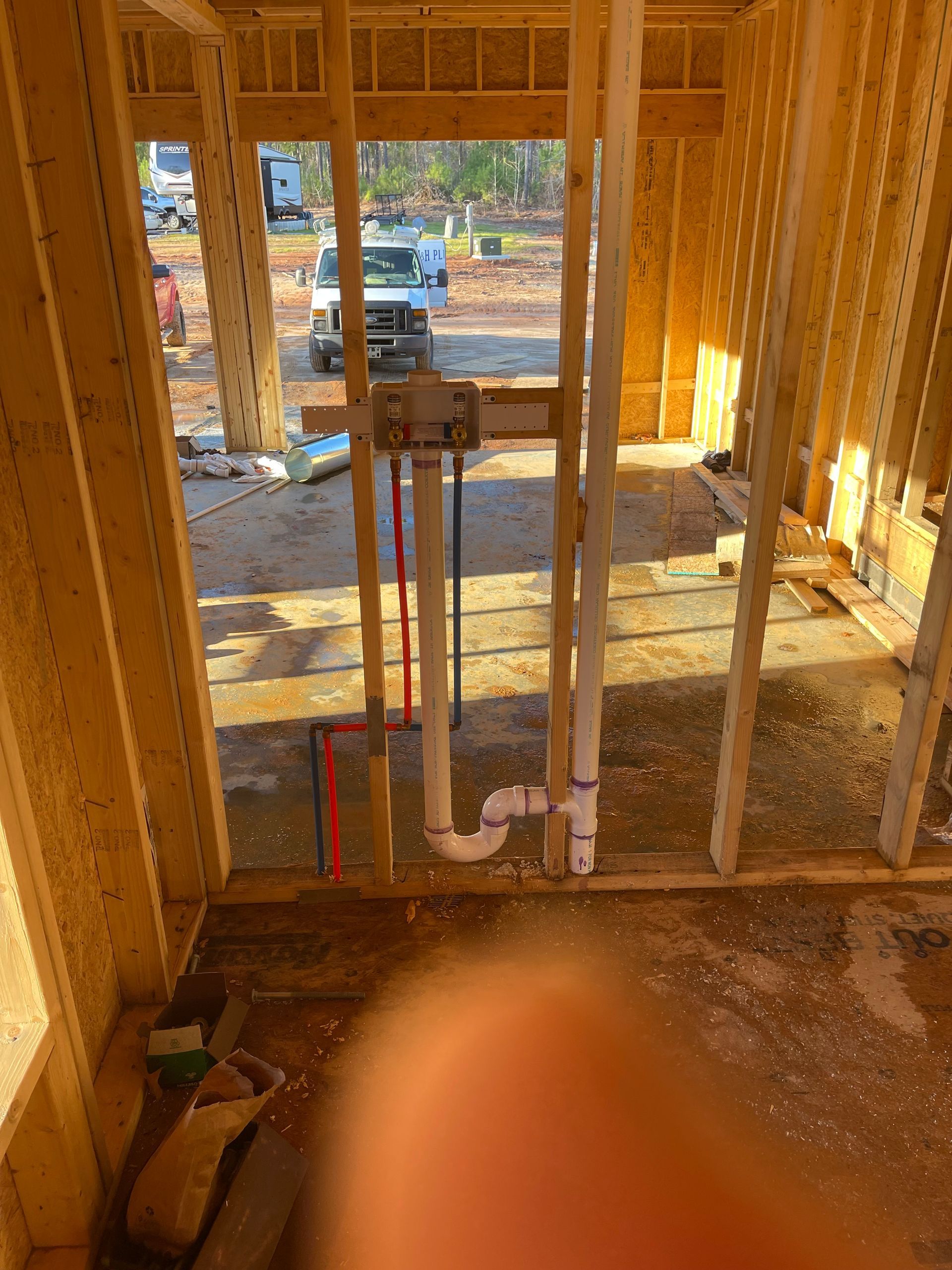 Interior of a framed house under construction with exposed plumbing pipes in the foreground.