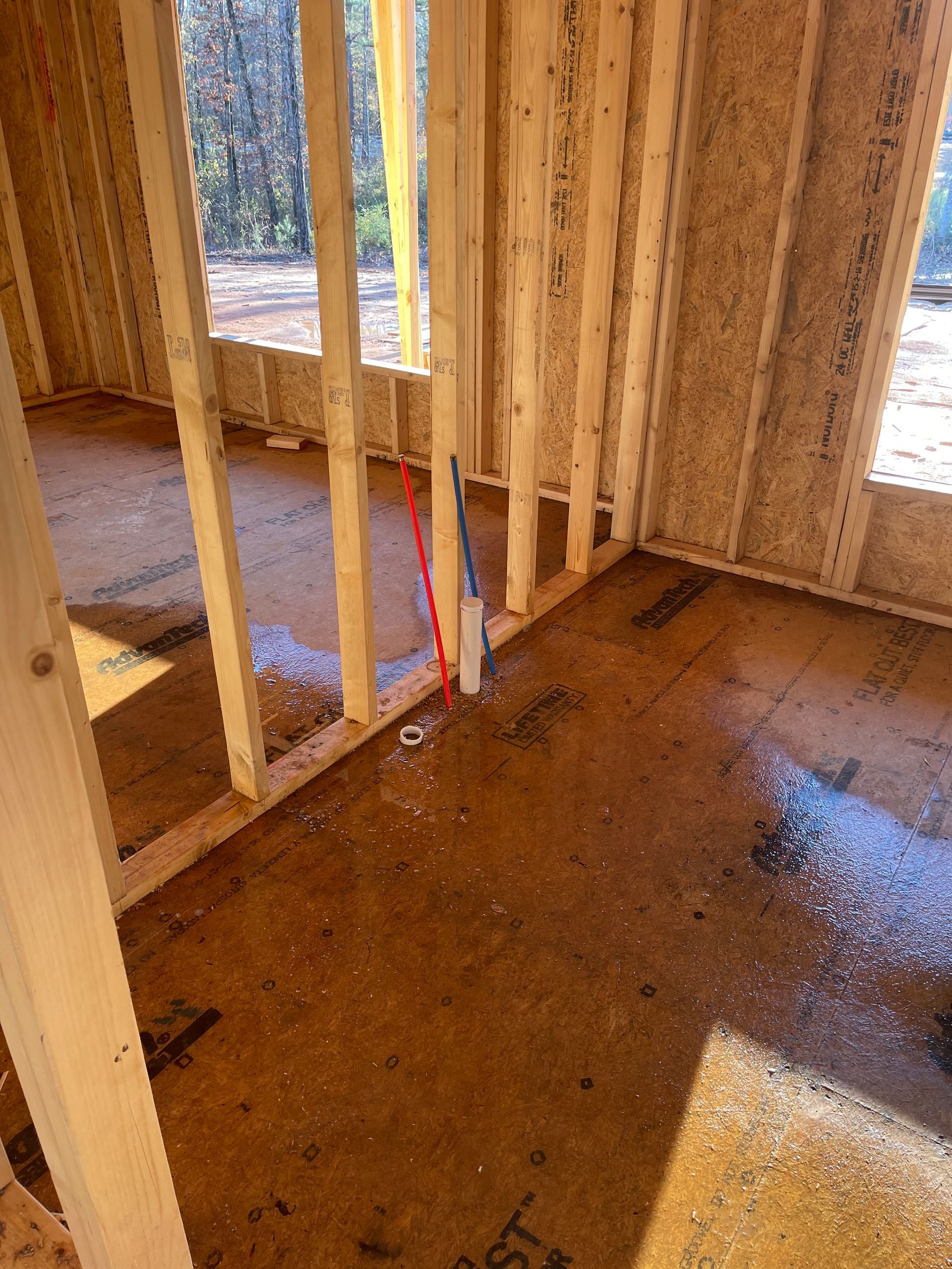 Interior of a framed room under construction with a window, exposed studs, and a concrete floor.
