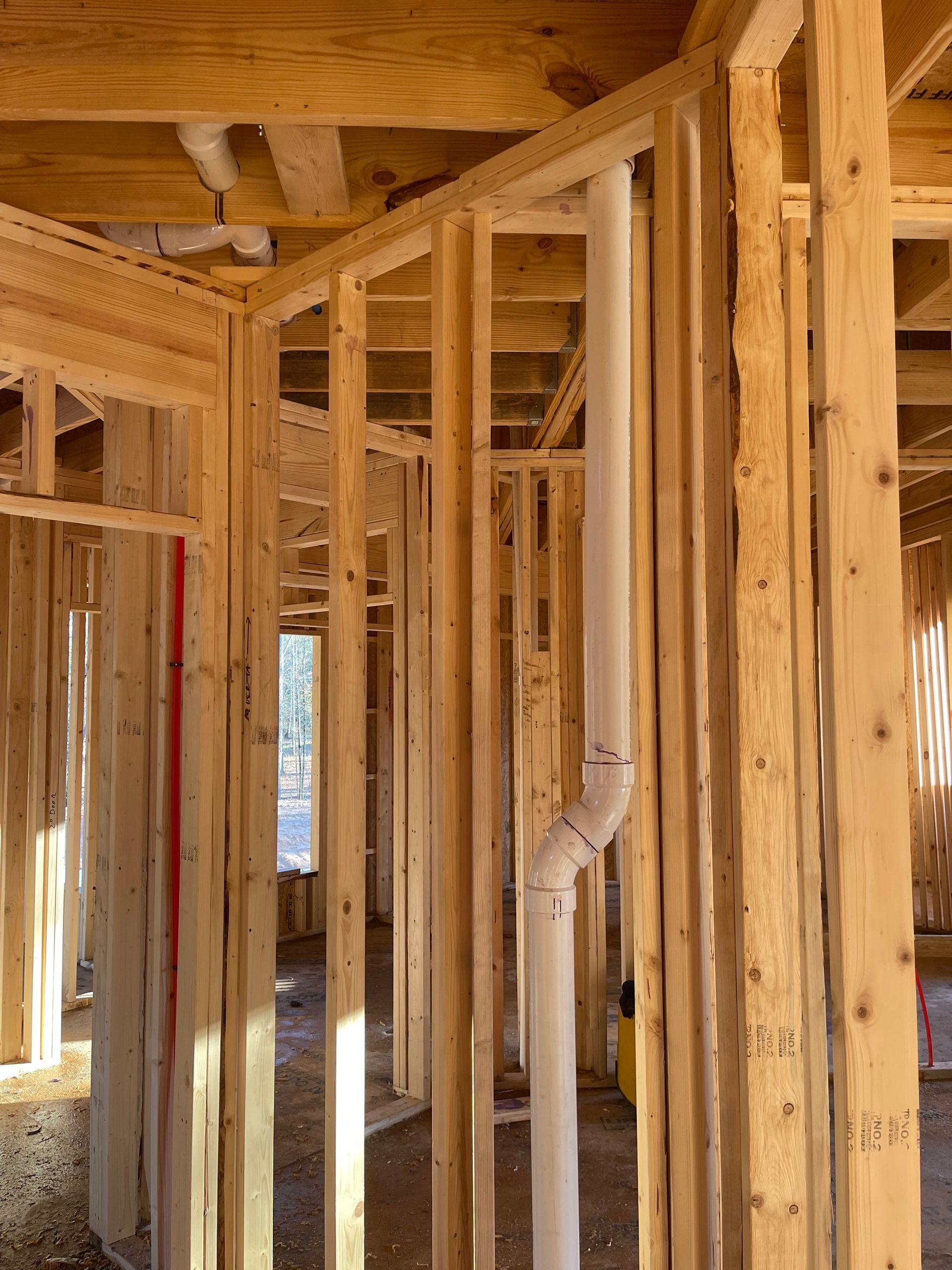 Unfinished wooden house framing with exposed studs, beams, and ductwork inside a construction site.