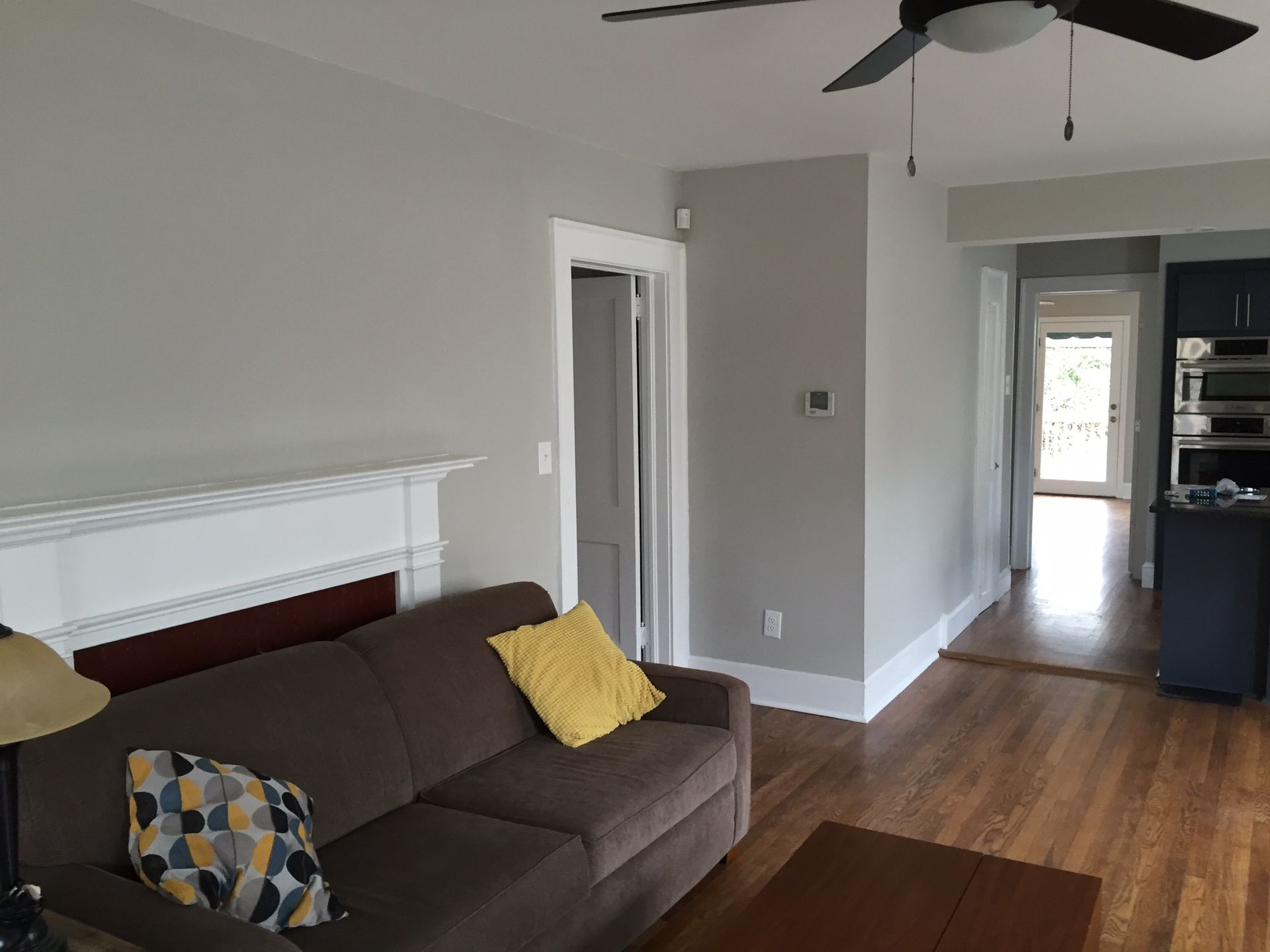 Living room with brown sofa, white fireplace, hardwood floors, and a hallway view beyond.