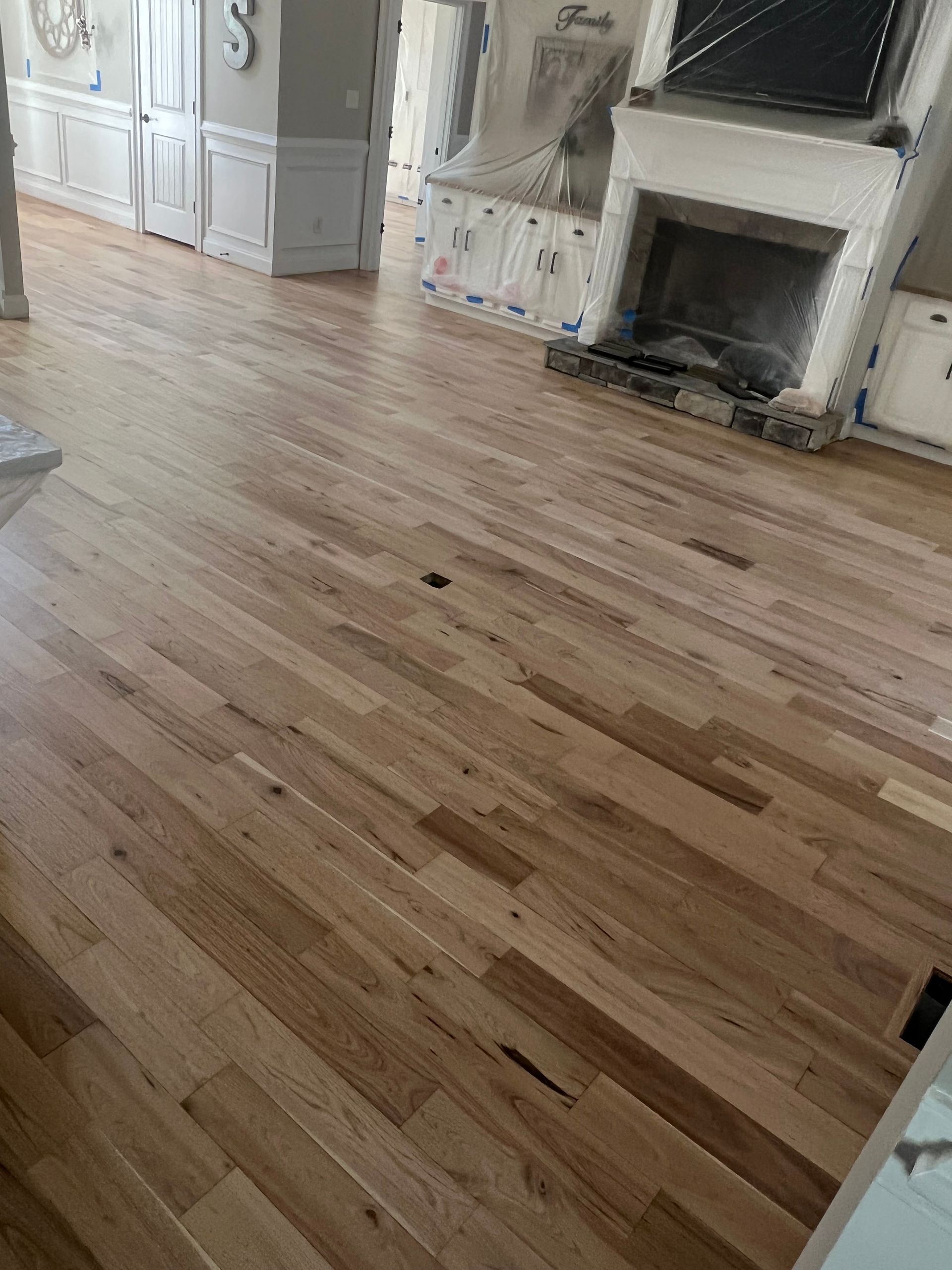 Empty hardwood-floored living room with a white fireplace and light-colored built-in cabinets.