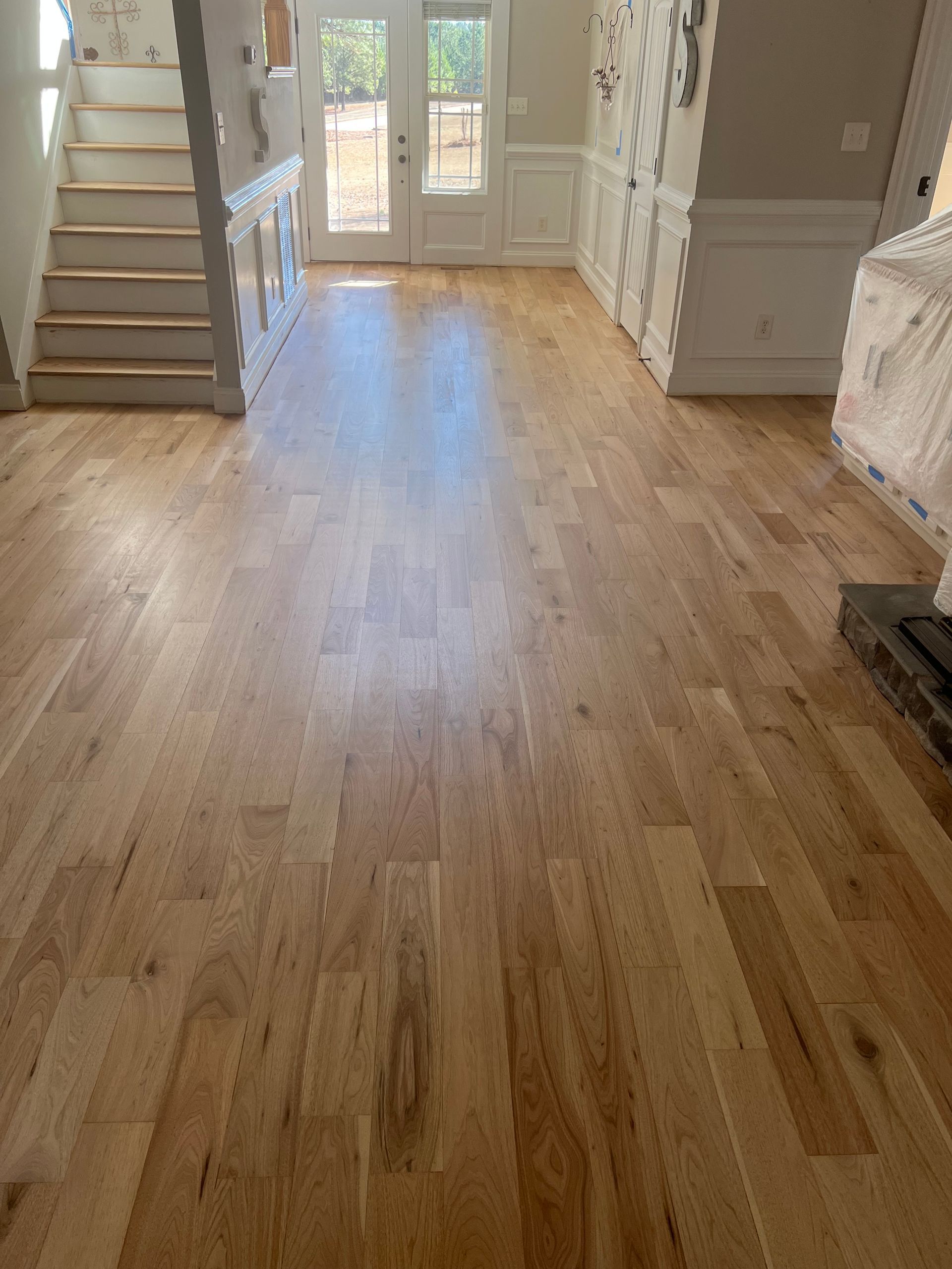 Bright hardwood-floored room with stairs, white built-ins, and glass doors at the back