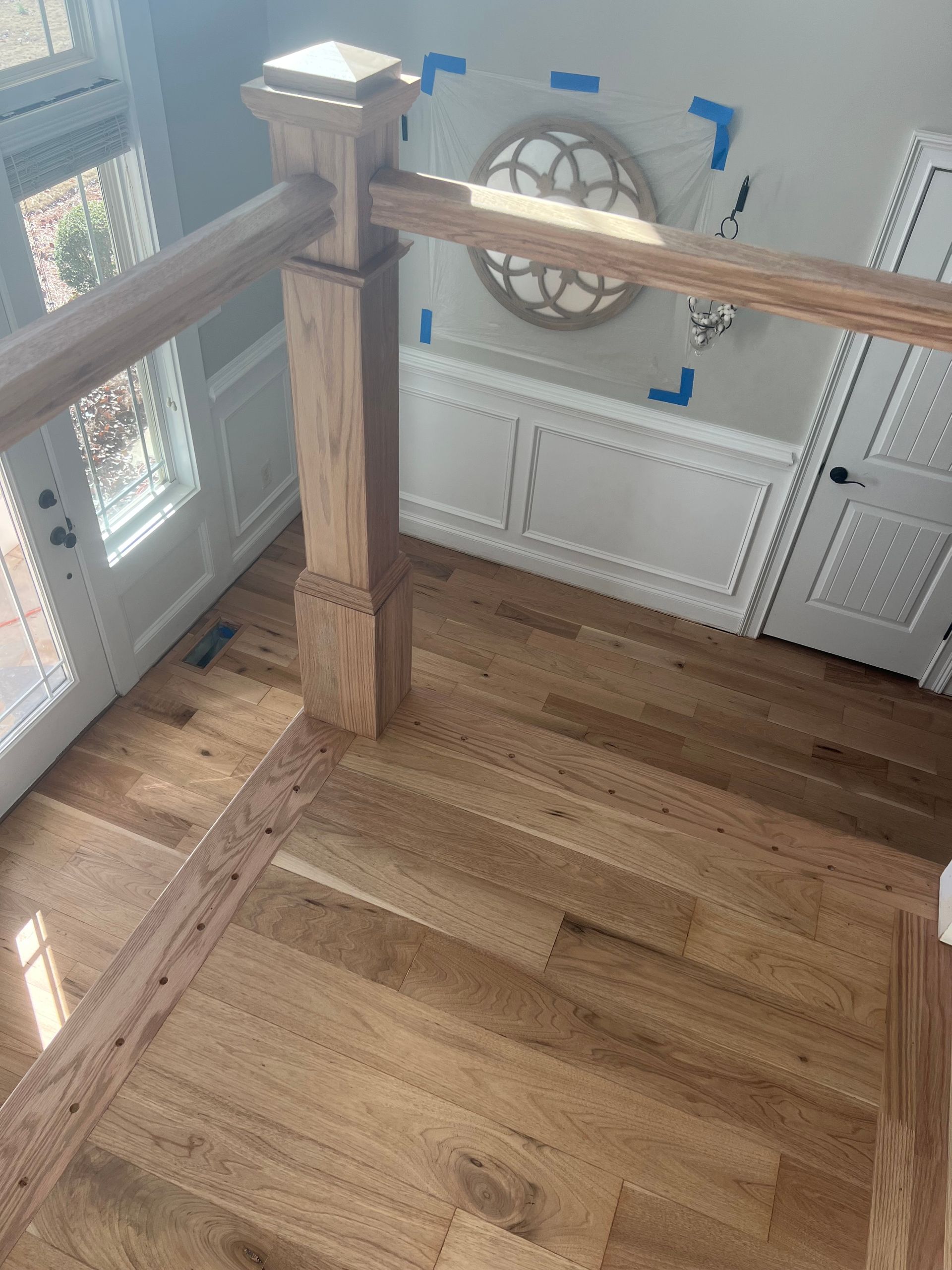 Wooden staircase railing by a window, with blue tape markers and a white built-in cabinet wall behind it