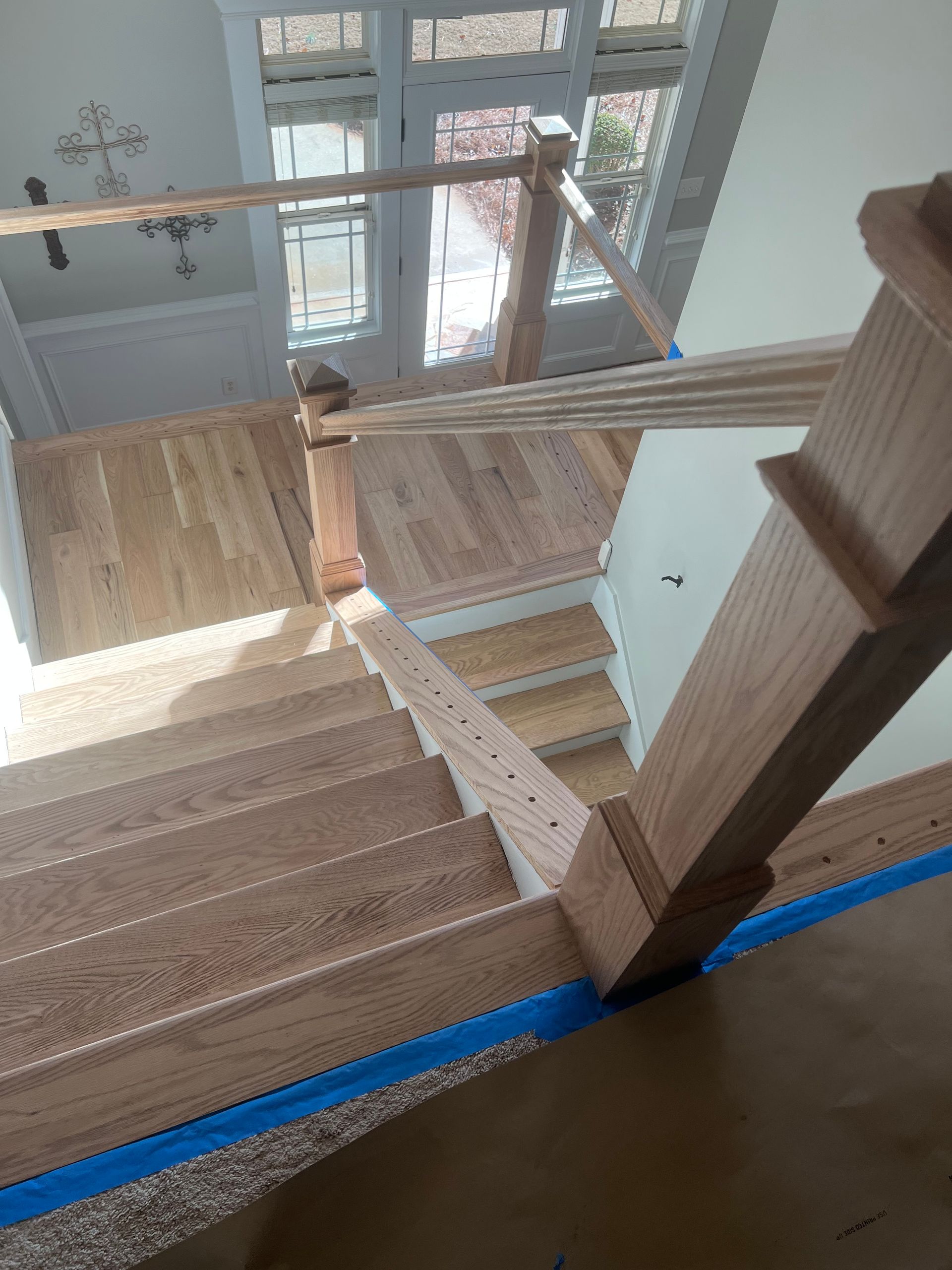 Staircase with carpeted steps, wooden railings, and a glass landing overlooking an entryway below