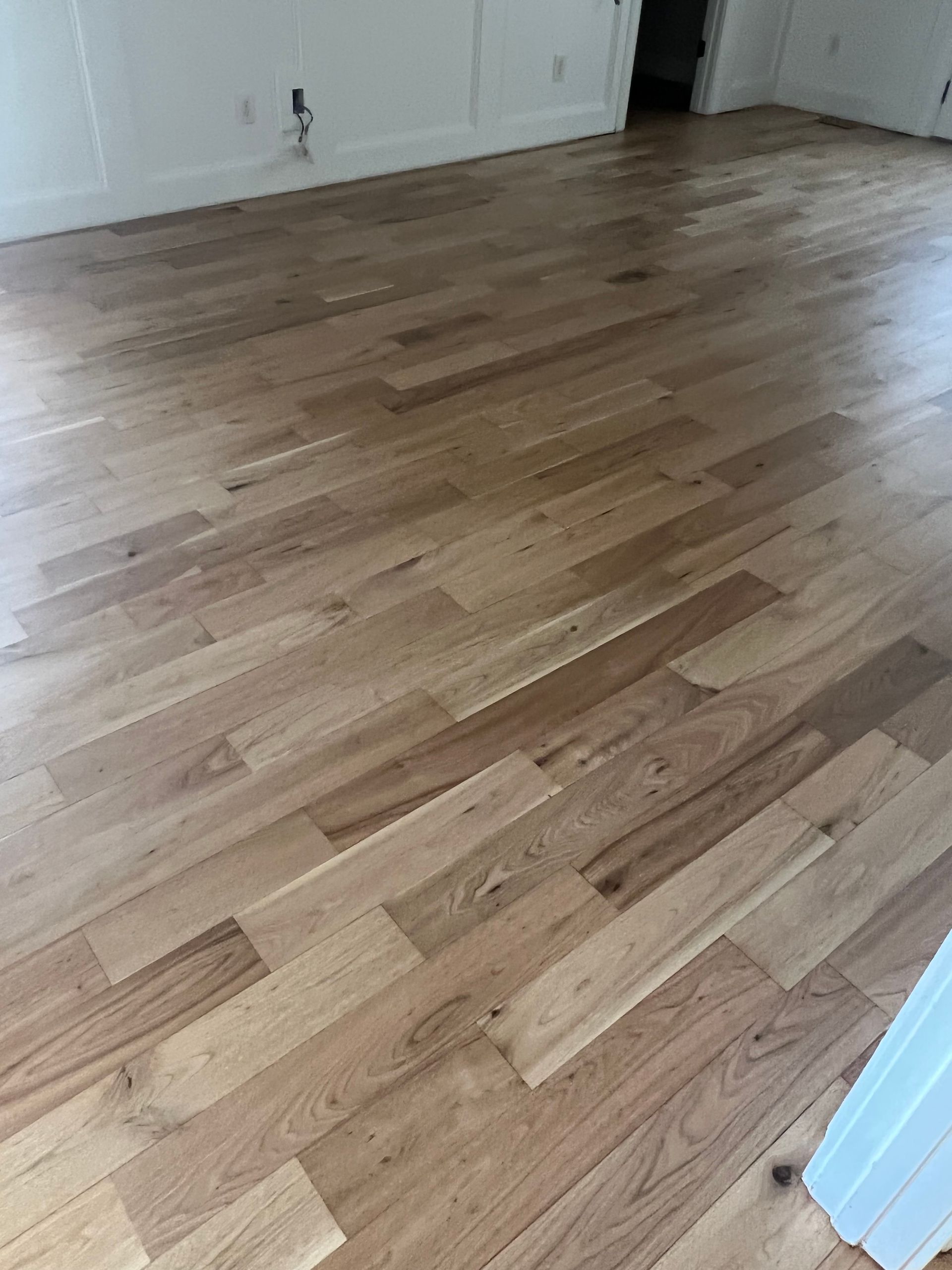 Empty room with light hardwood flooring and white walls, viewed from a doorway