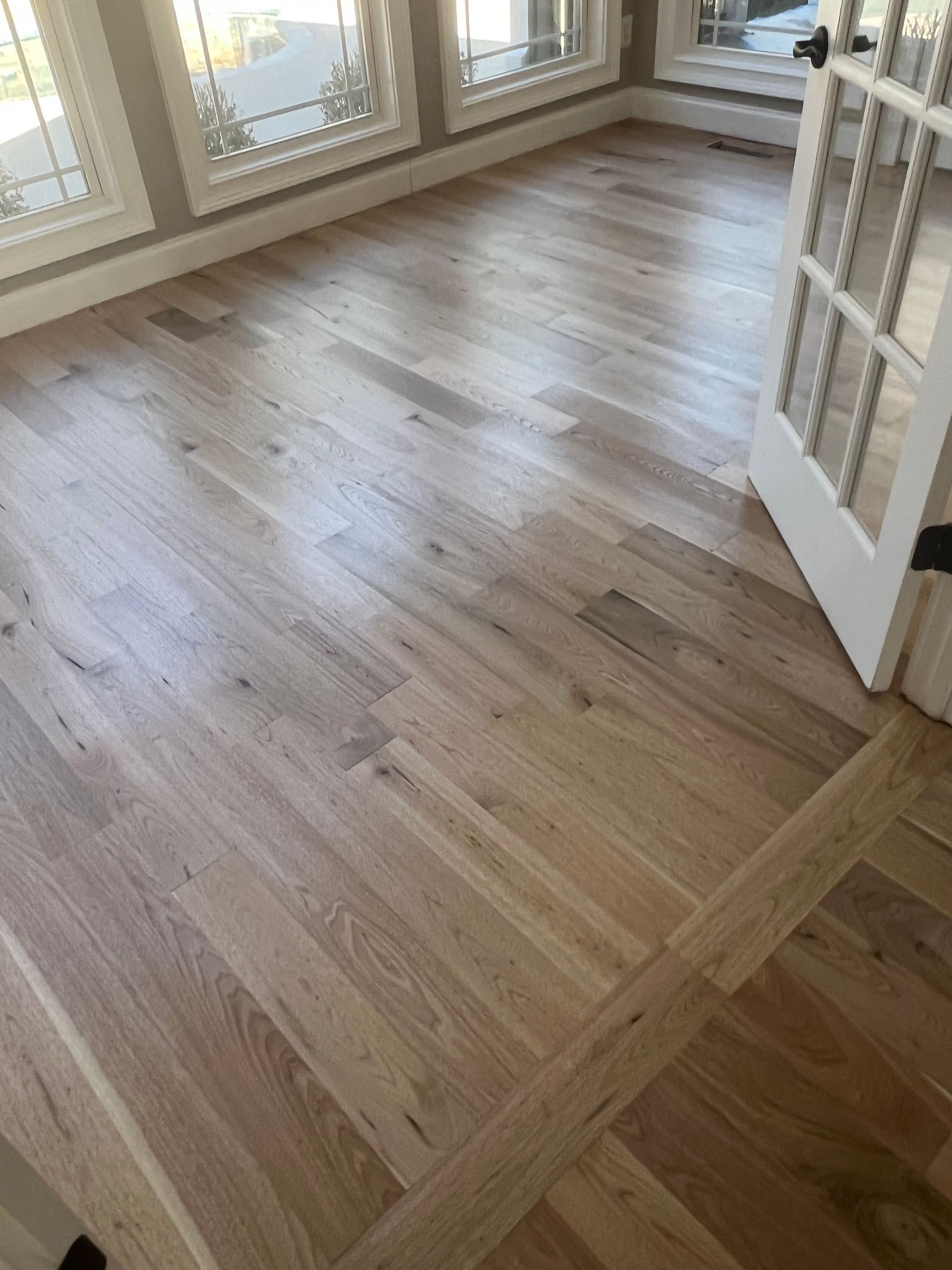 Sunlit hardwood-floored room with windows and a white French door