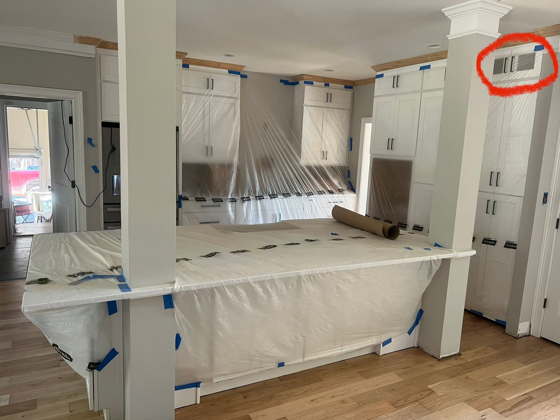 Plastic-covered kitchen under renovation with white cabinets, central island, and wood floors