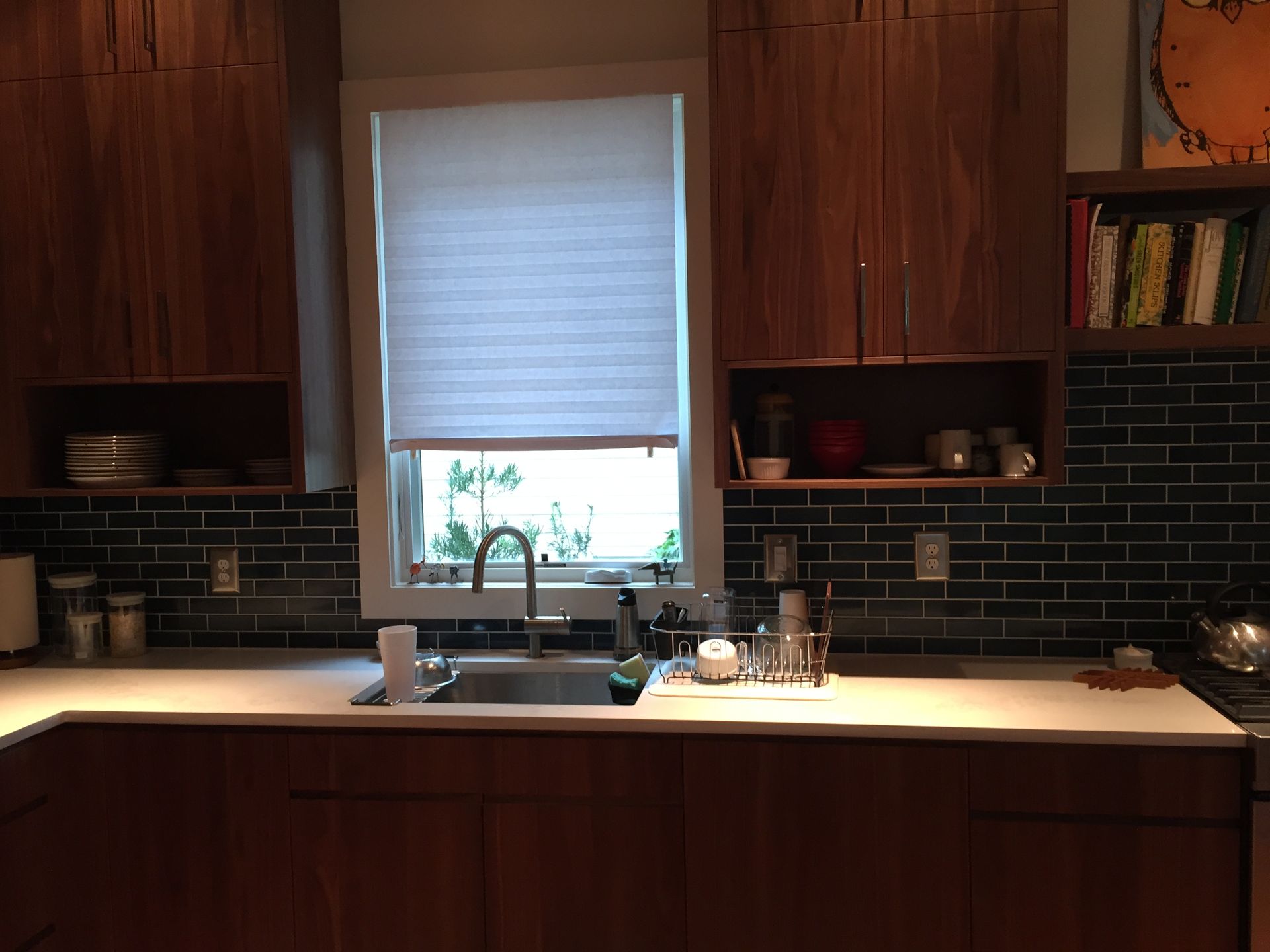 Kitchen with wood cabinets, dark tile backsplash, white countertops, and a window over the sink.