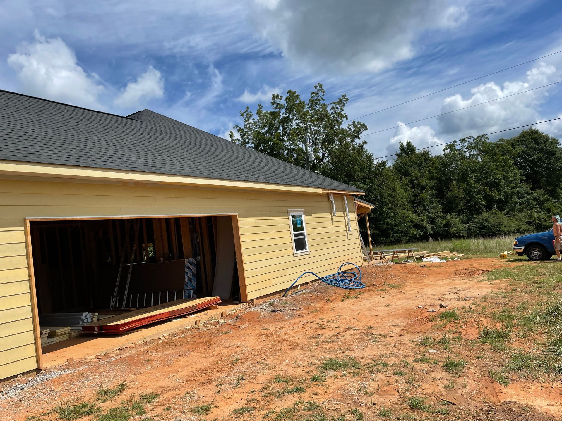 Yellow house under construction with open garage, dirt yard, and cloudy sky
