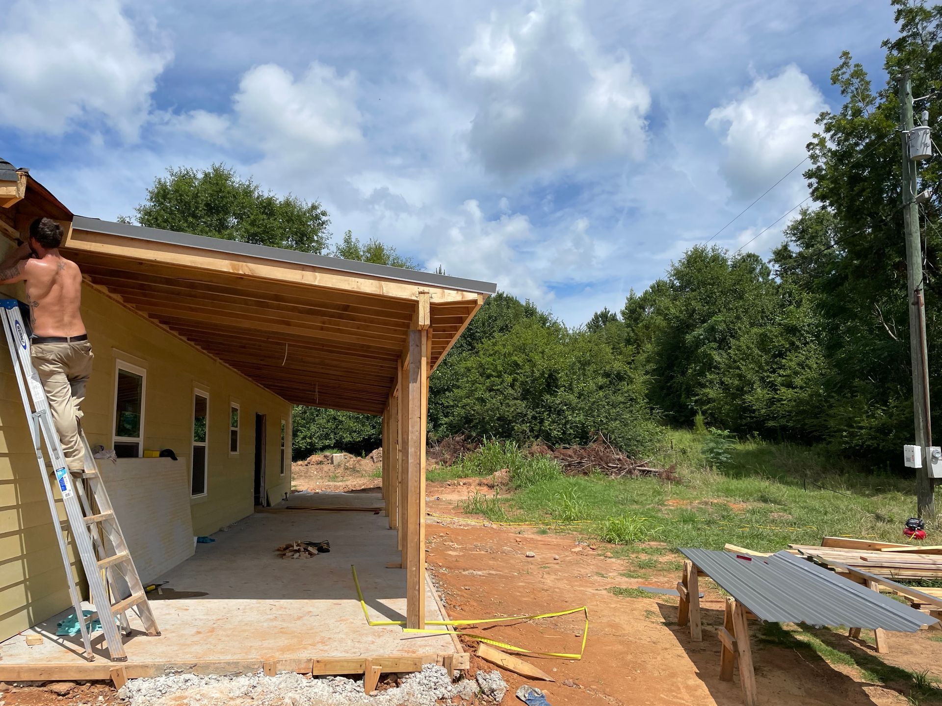 House under construction with covered porch, ladder, and building materials in a yard
