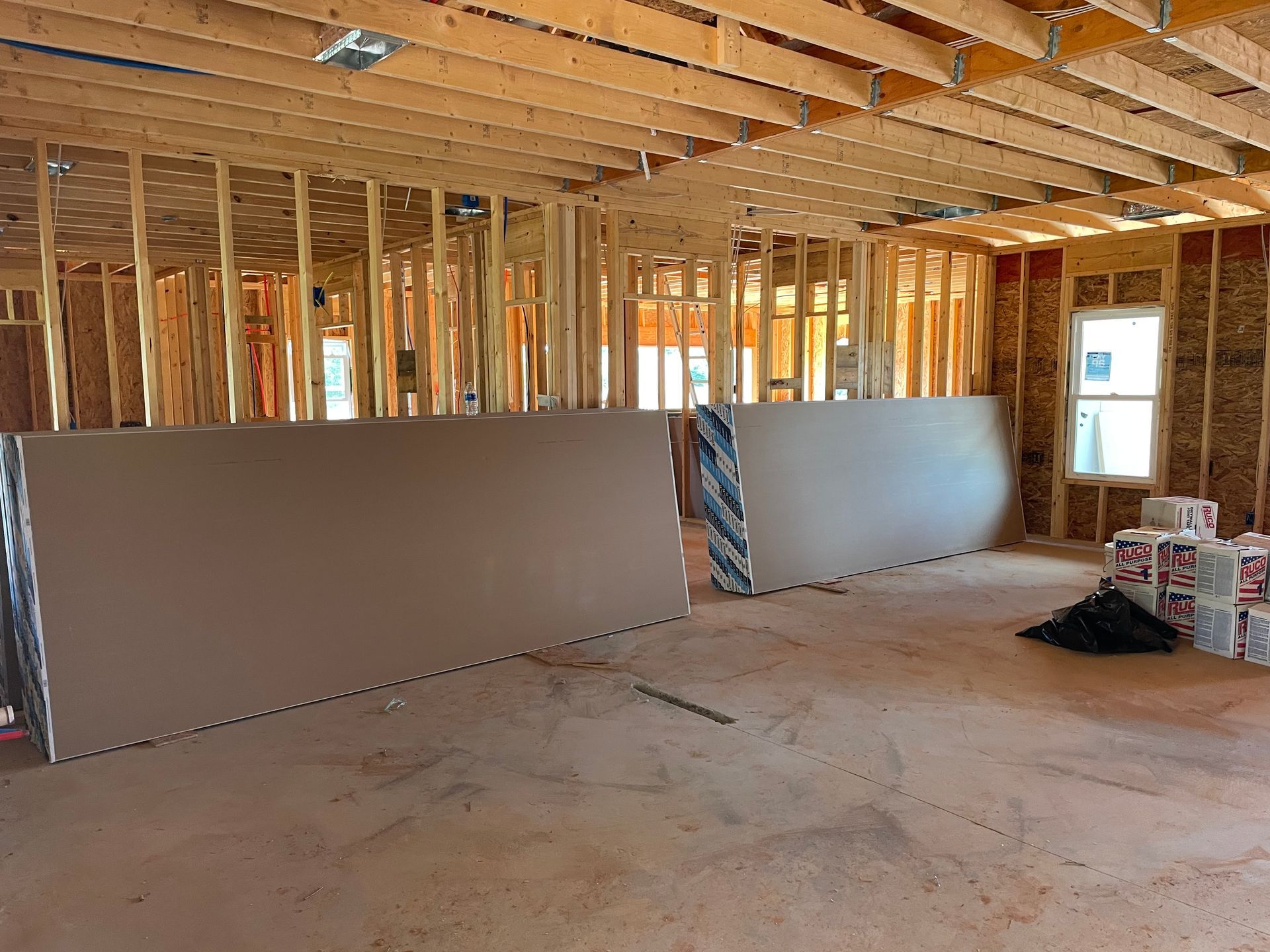 Unfinished interior framing with drywall panels leaning against wood studs and a dusty floor