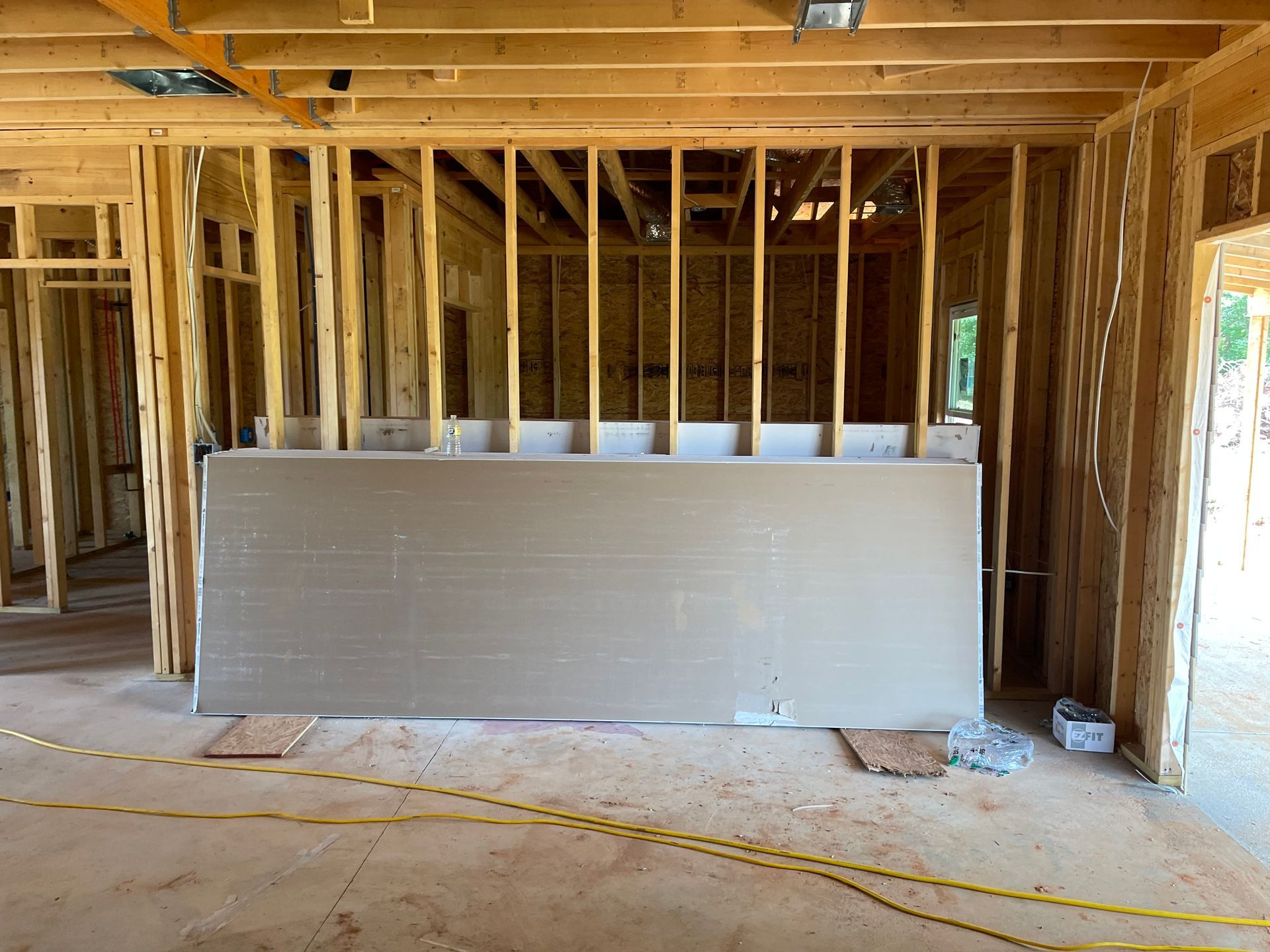 Interior of a framed house under construction with drywall stacked against wall studs and exposed ceiling joists