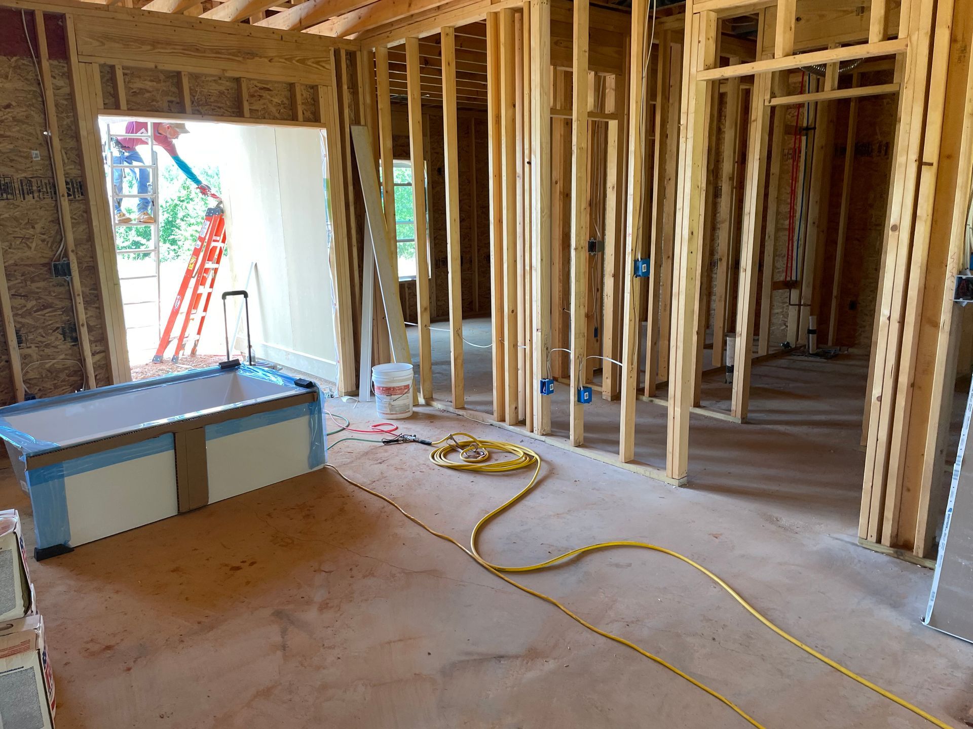 Framed house interior under construction with exposed studs, a stepladder by the doorway, and a blue toolbox on the floor