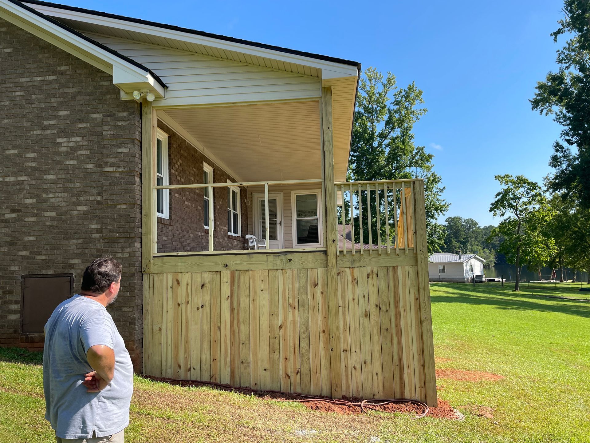 Man standing in a yard looking at a newly built wooden porch addition on a brick house