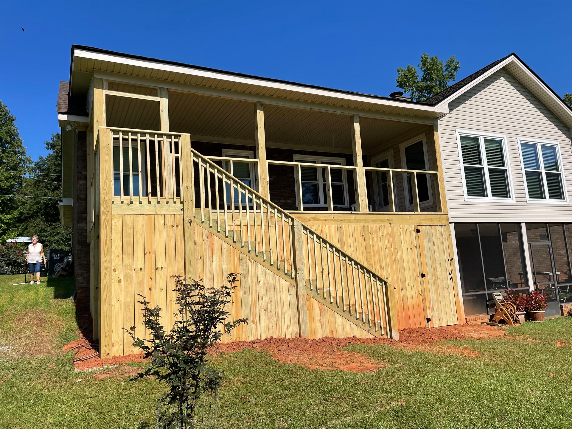 Wooden front porch addition on a house with tan siding and stairs, under a blue sky