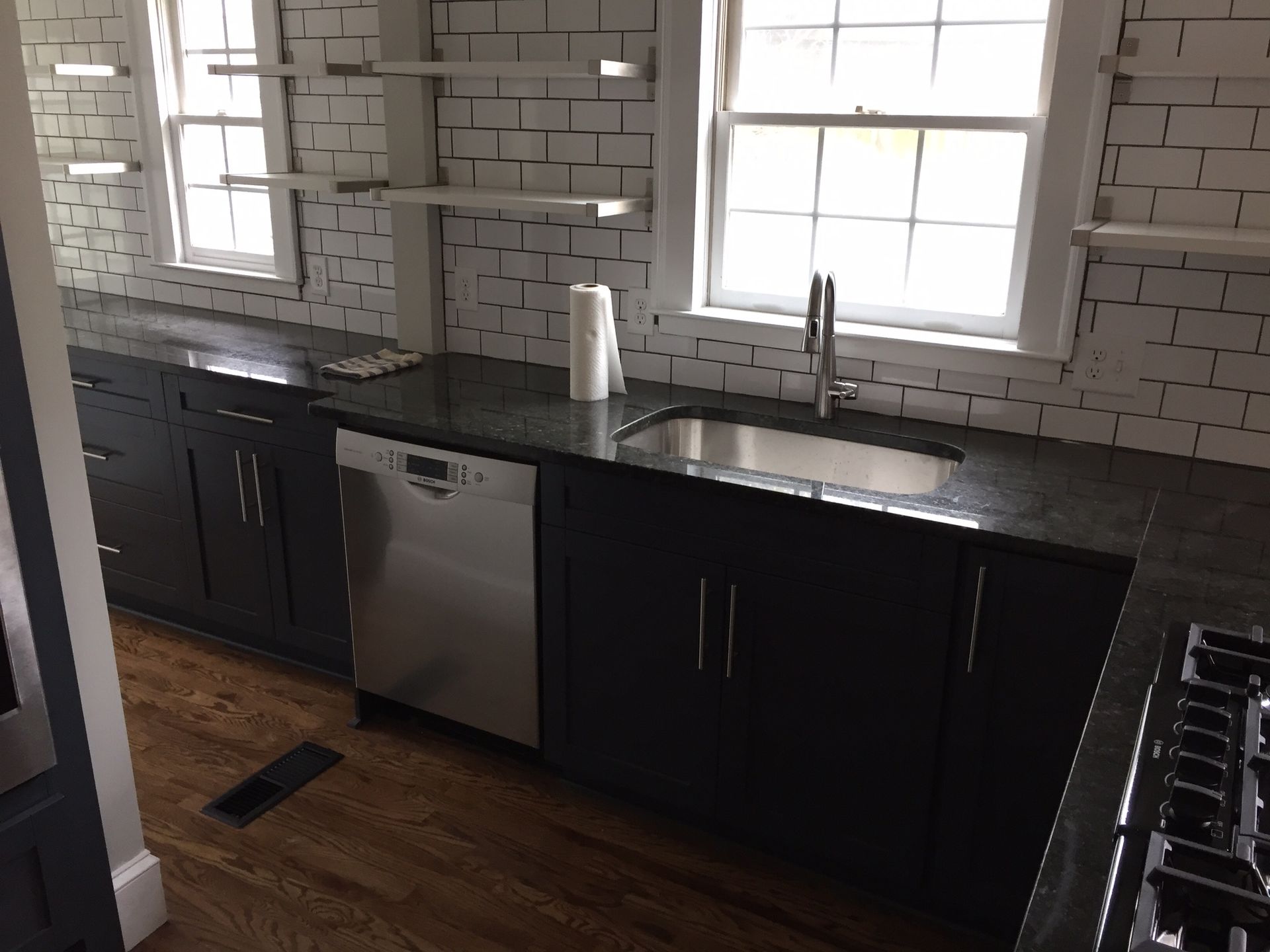 Modern kitchen with black cabinets, stainless dishwasher, white subway tile backsplash, and large windows.