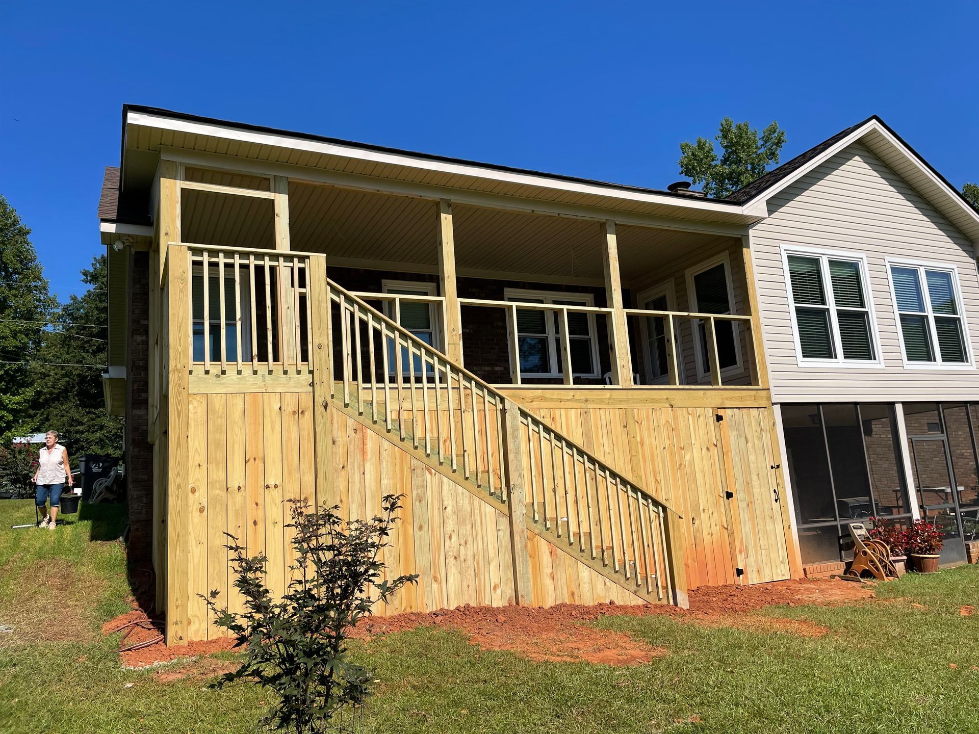 Front porch under construction on a tan house with wood siding and a railing, beside a white house.