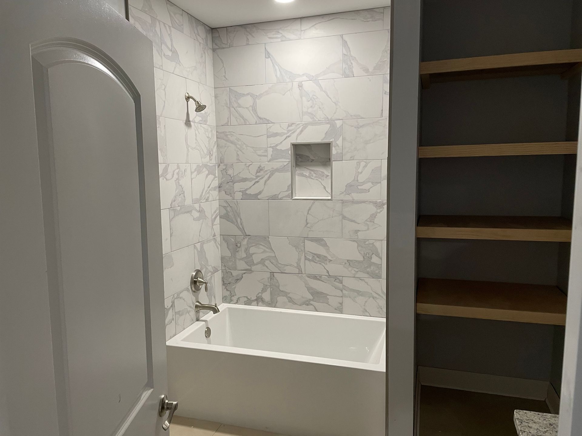 Small bathroom with bathtub, tiled shower wall, and open shelving alcove