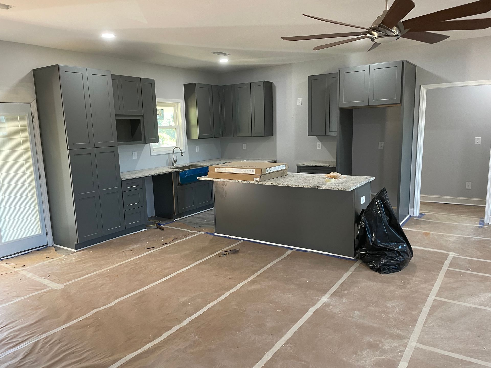 Renovated kitchen with gray cabinets, island, and covered floor during construction