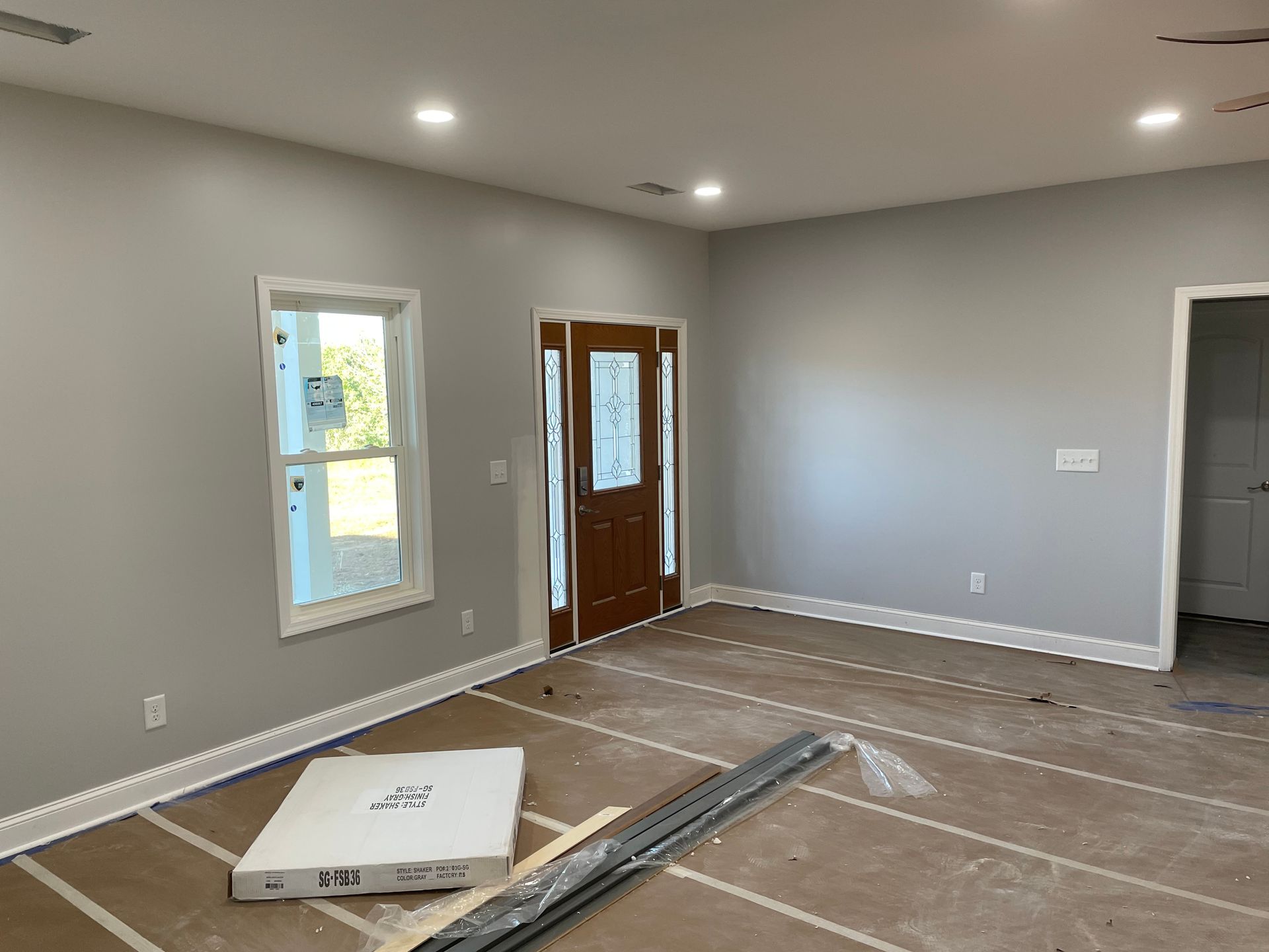 Empty living room under renovation with gray walls, recessed lights, and flooring materials on the floor