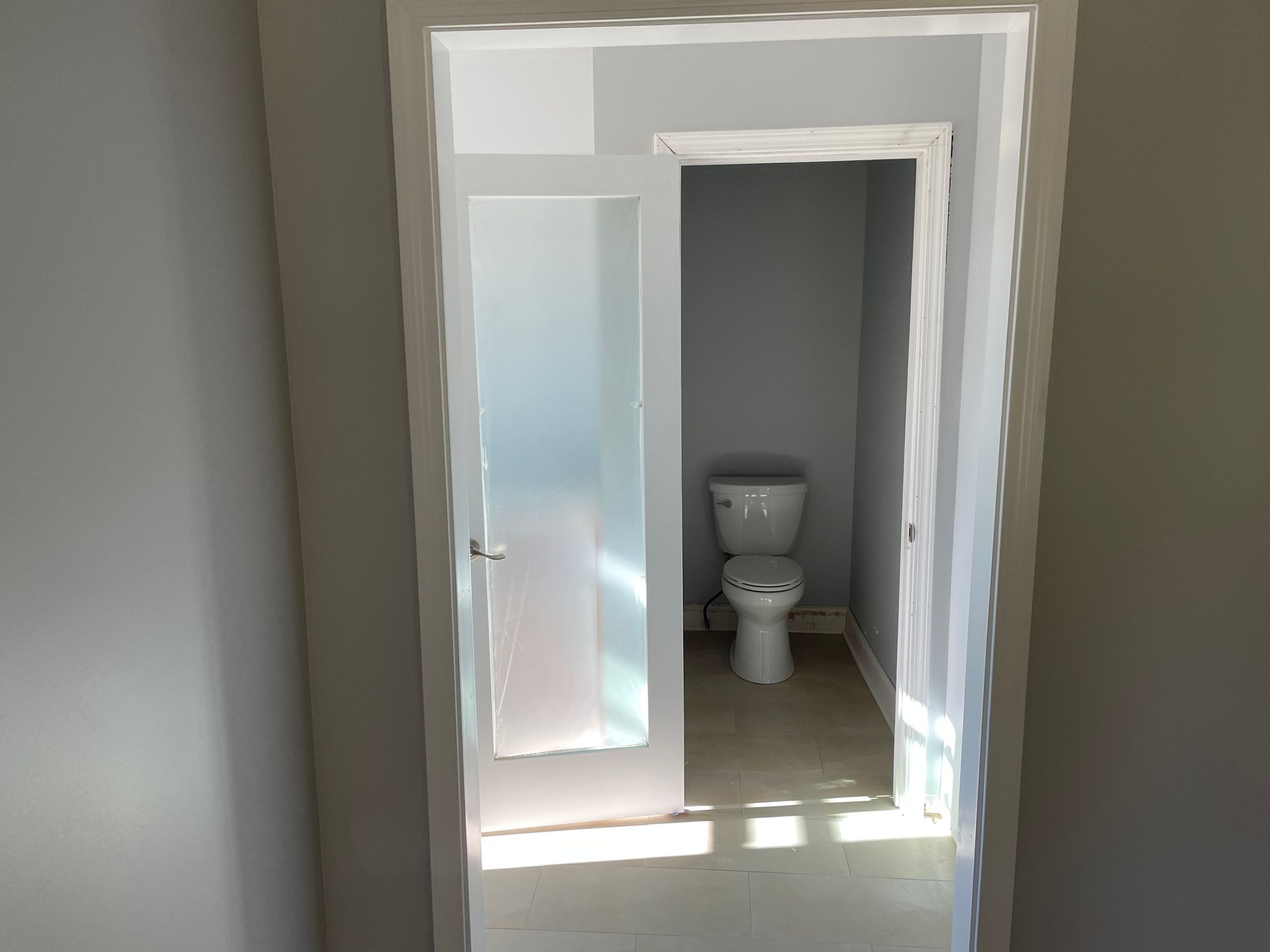 Open doorway to a small bathroom with a white toilet and frosted glass door.