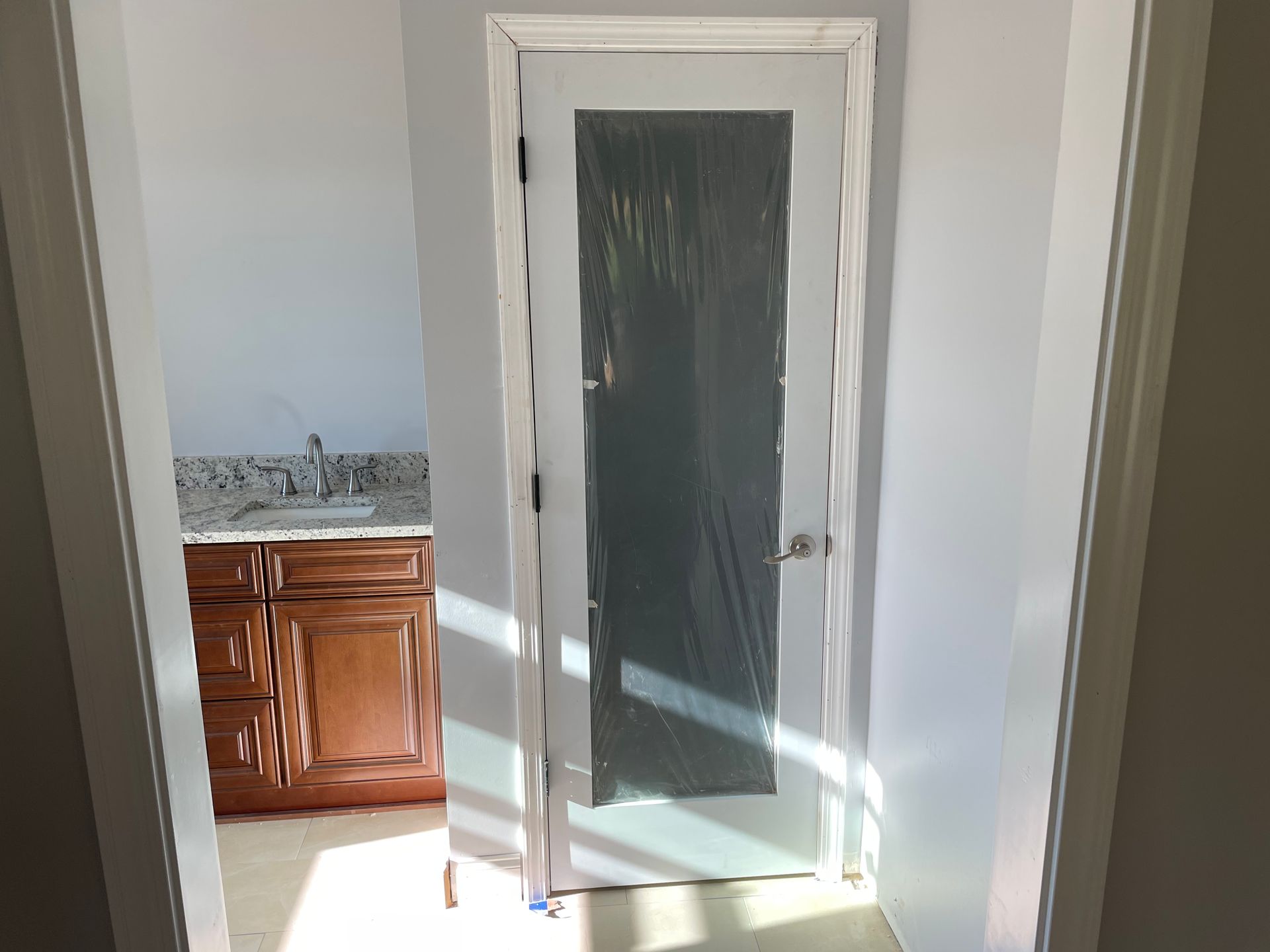 Glass door with white trim in a bright hallway, leading to a kitchen with wooden cabinets