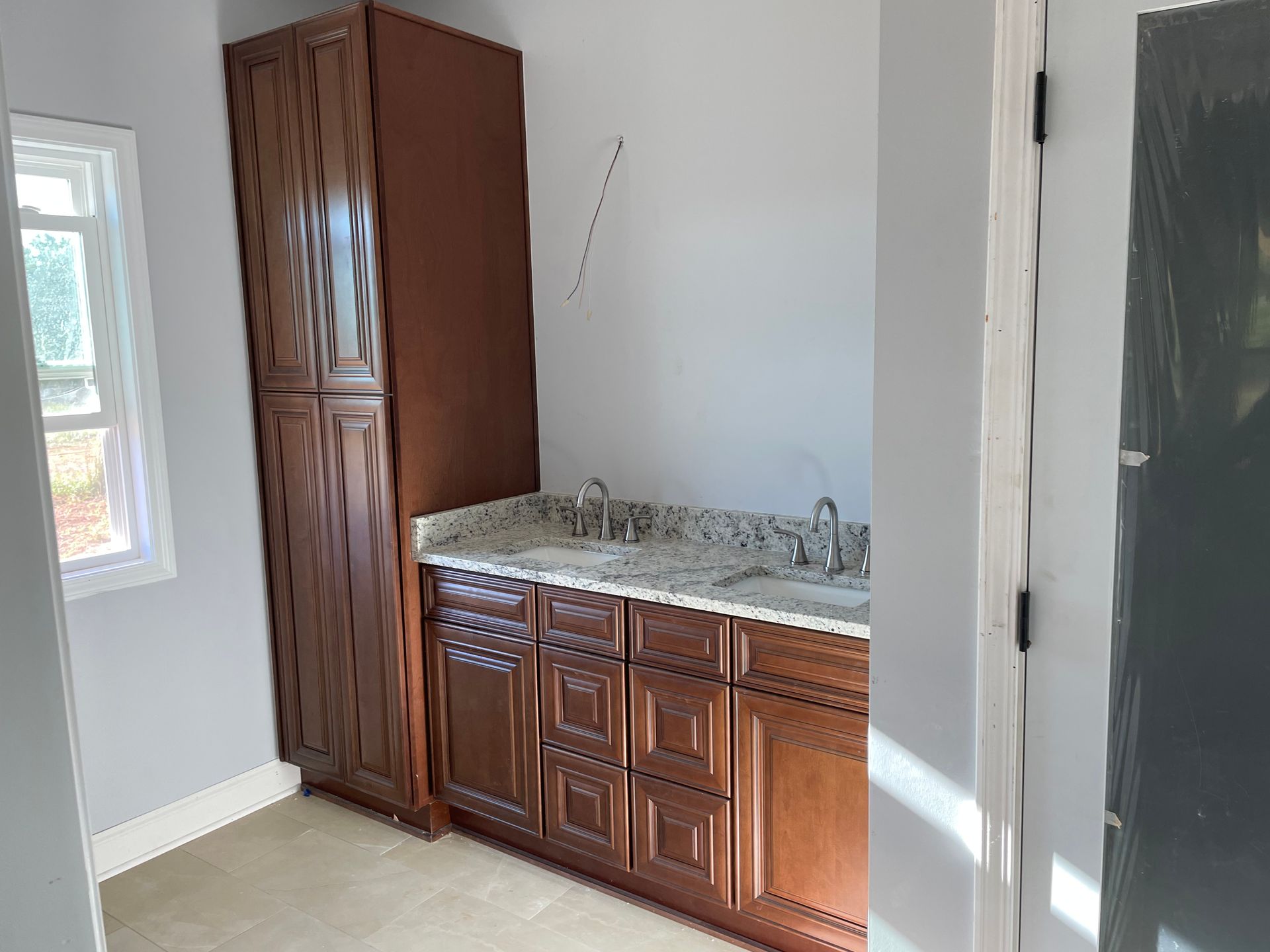 Bathroom vanity with wood cabinets, granite countertop, and a tall storage cabinet in a bright room