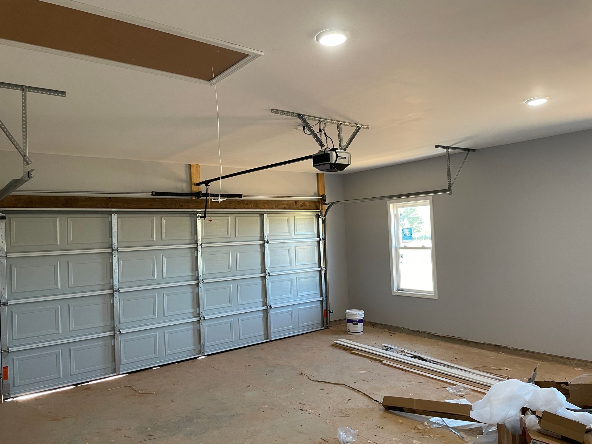 Empty garage interior with closed sectional door, gray walls, ceiling lights, and garage door opener rails.