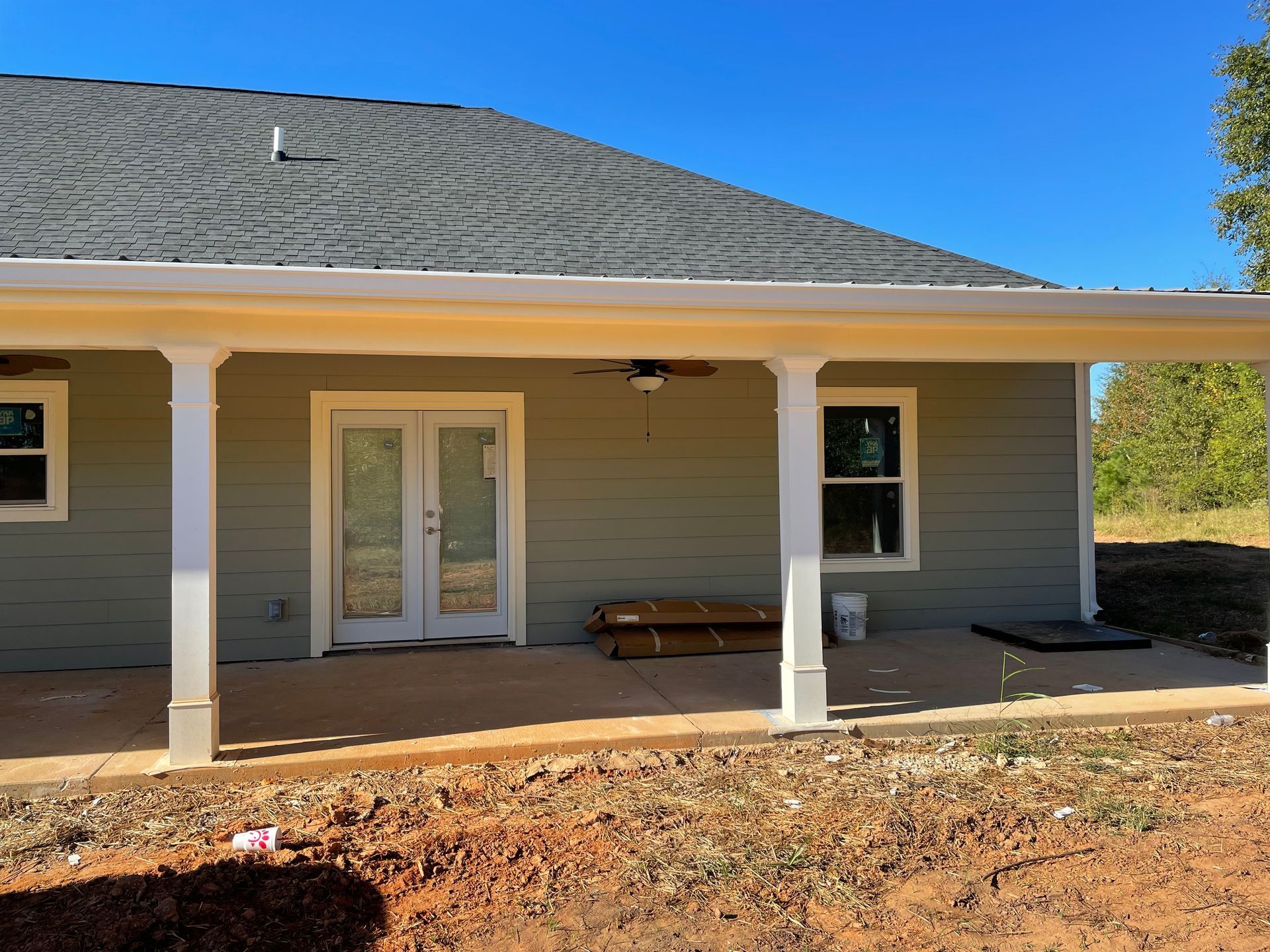 Front porch of a gray house with white columns, double doors, and a bench in sunlight