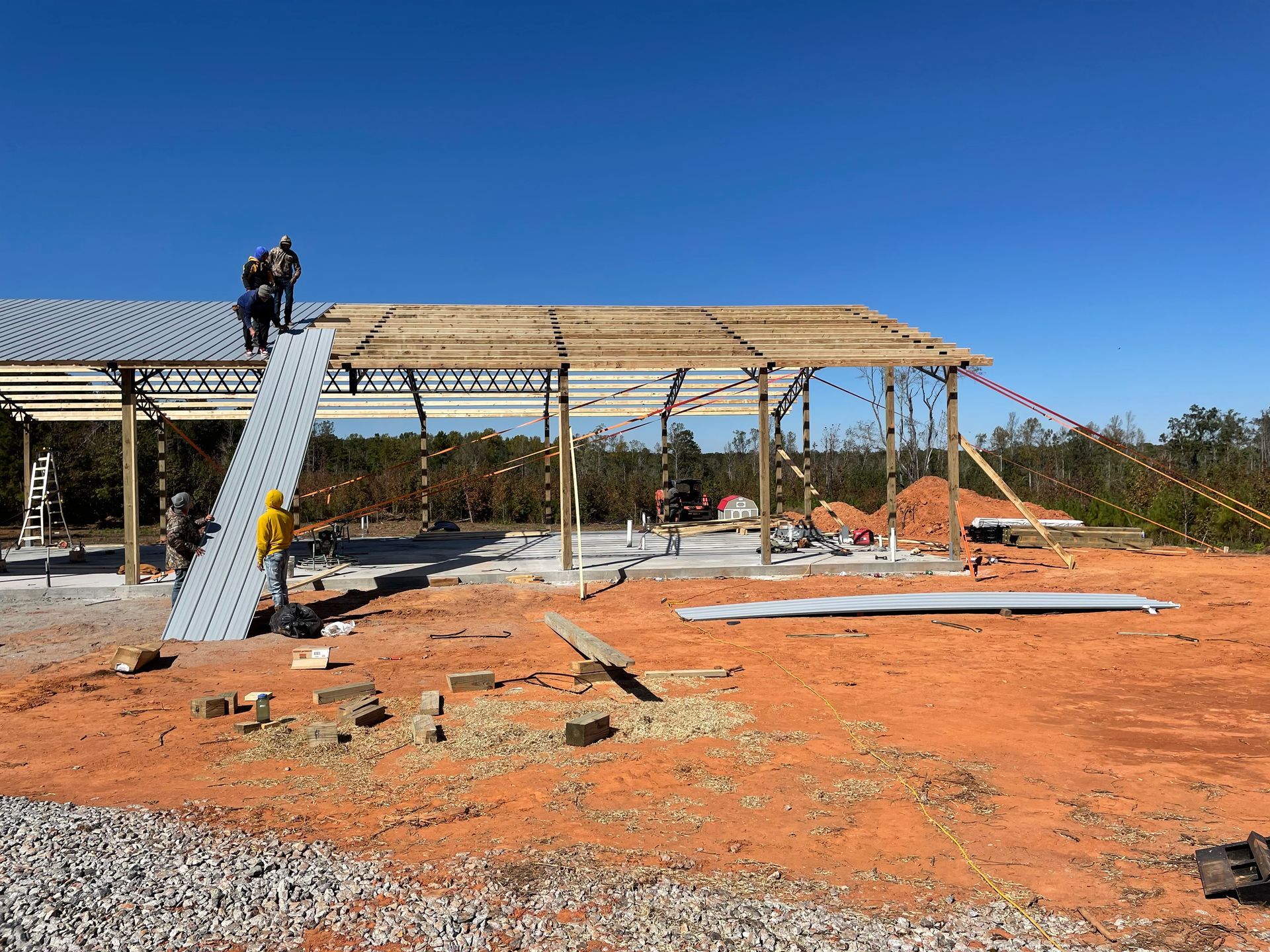 Construction site with metal frame, worker on ladder, and red dirt under a clear blue sky