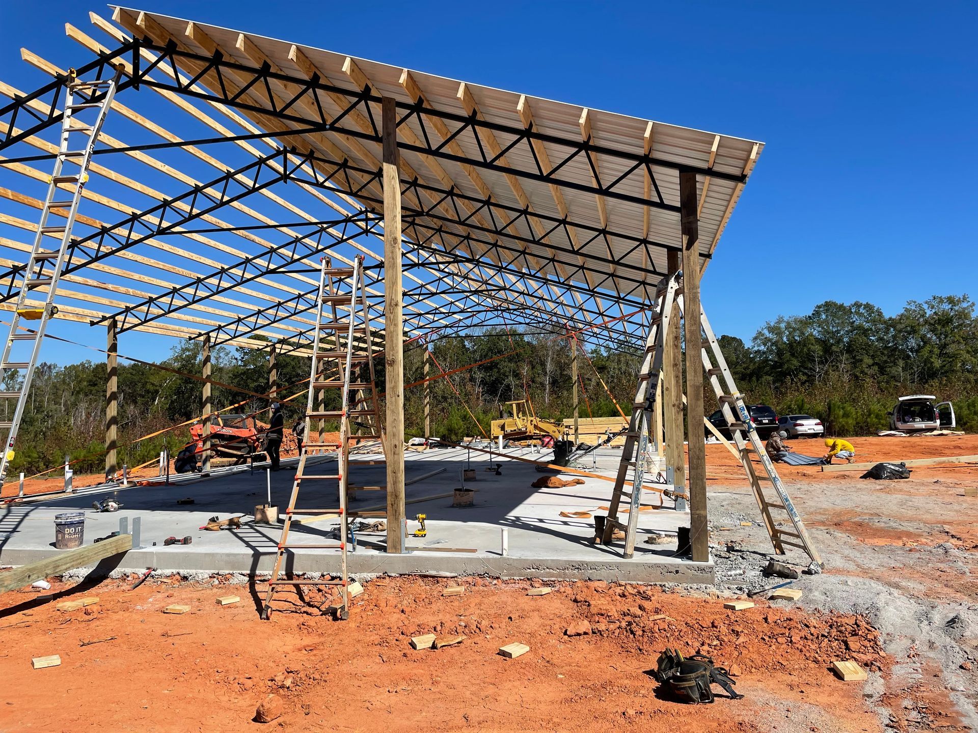 Partially built steel pavilion on a construction site with concrete slab and red dirt